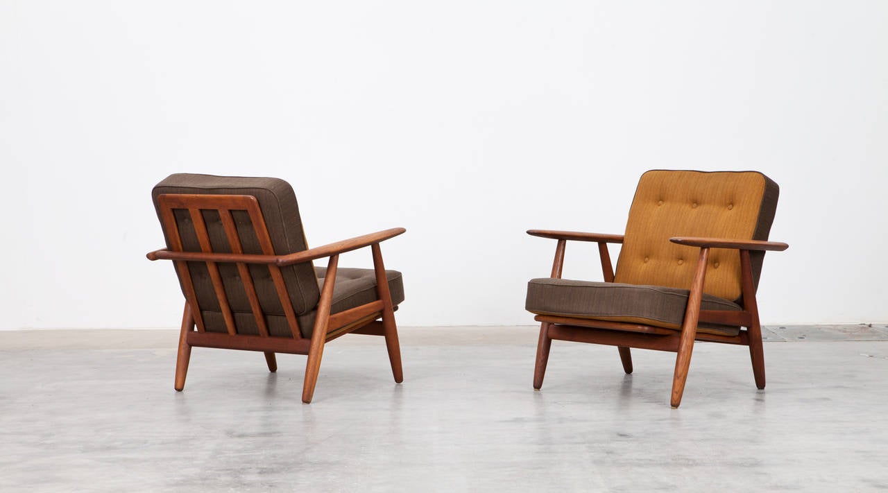 This couple of lounge chairs is designed by Hans Wegner. The chairs with their thick and qualitative cushions are very comfortable and appear in two colors. The base is made out of teak. Manufactured by GETAMA.
