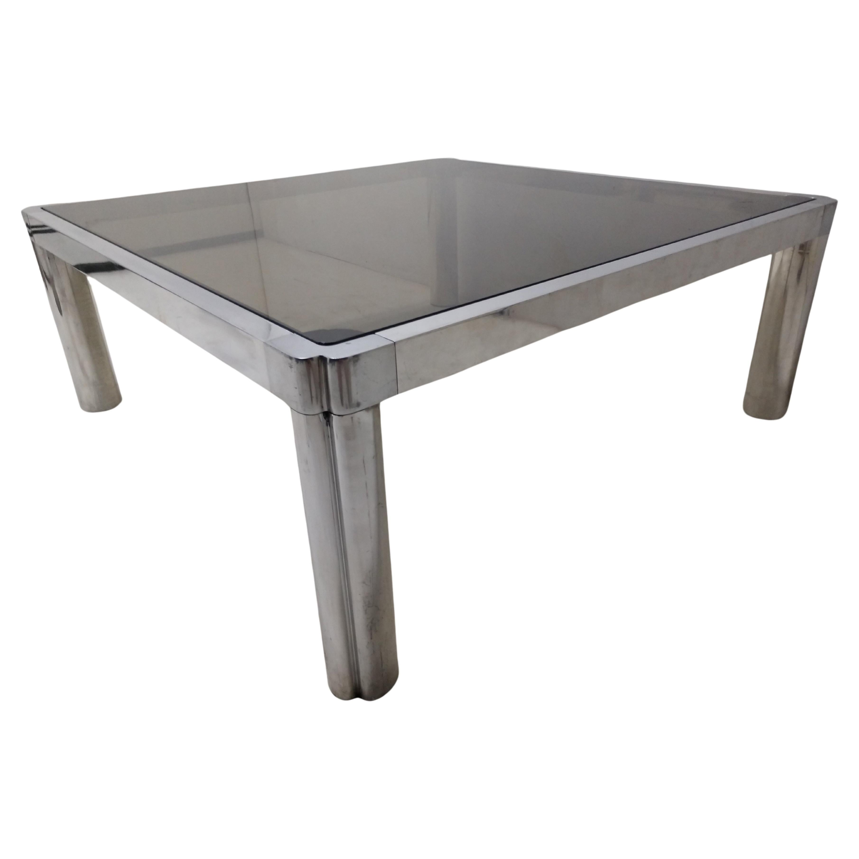 Fabulous cast aluminum cocktail table with a smoked glass top inset. Tube legs with flat bars connecting the sides. Well constructed piece as fittings are tight and precise. Some minimal scratches to both the frame and the glass. Rubber bumper
