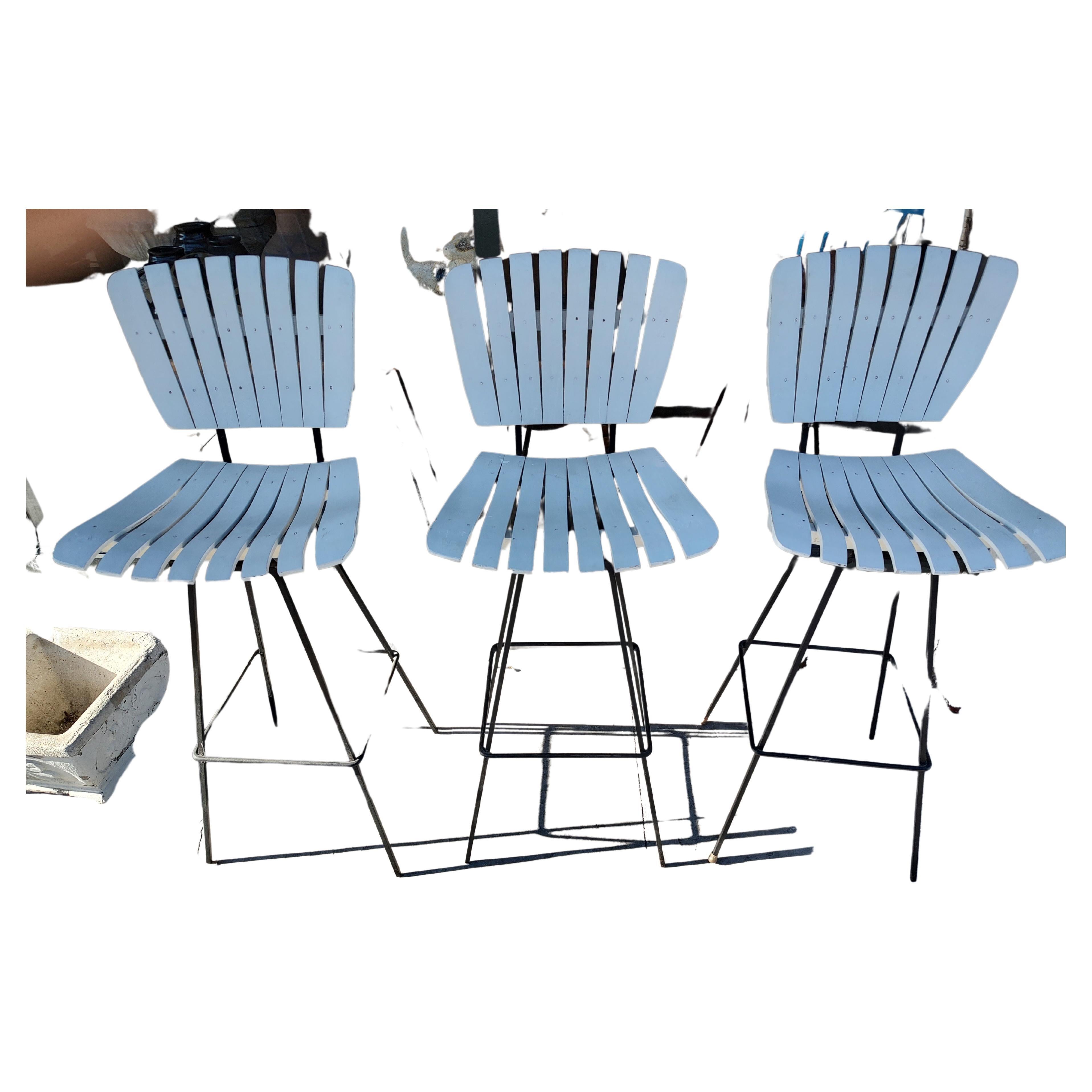 Fabulous set of 3 slatted bar stools believed to be Arthur Umanoff. Solid Iron bars which support the swiveling seats. Seats & back painted white. In excellent vintage condition with minimal wear with new rubber feet.