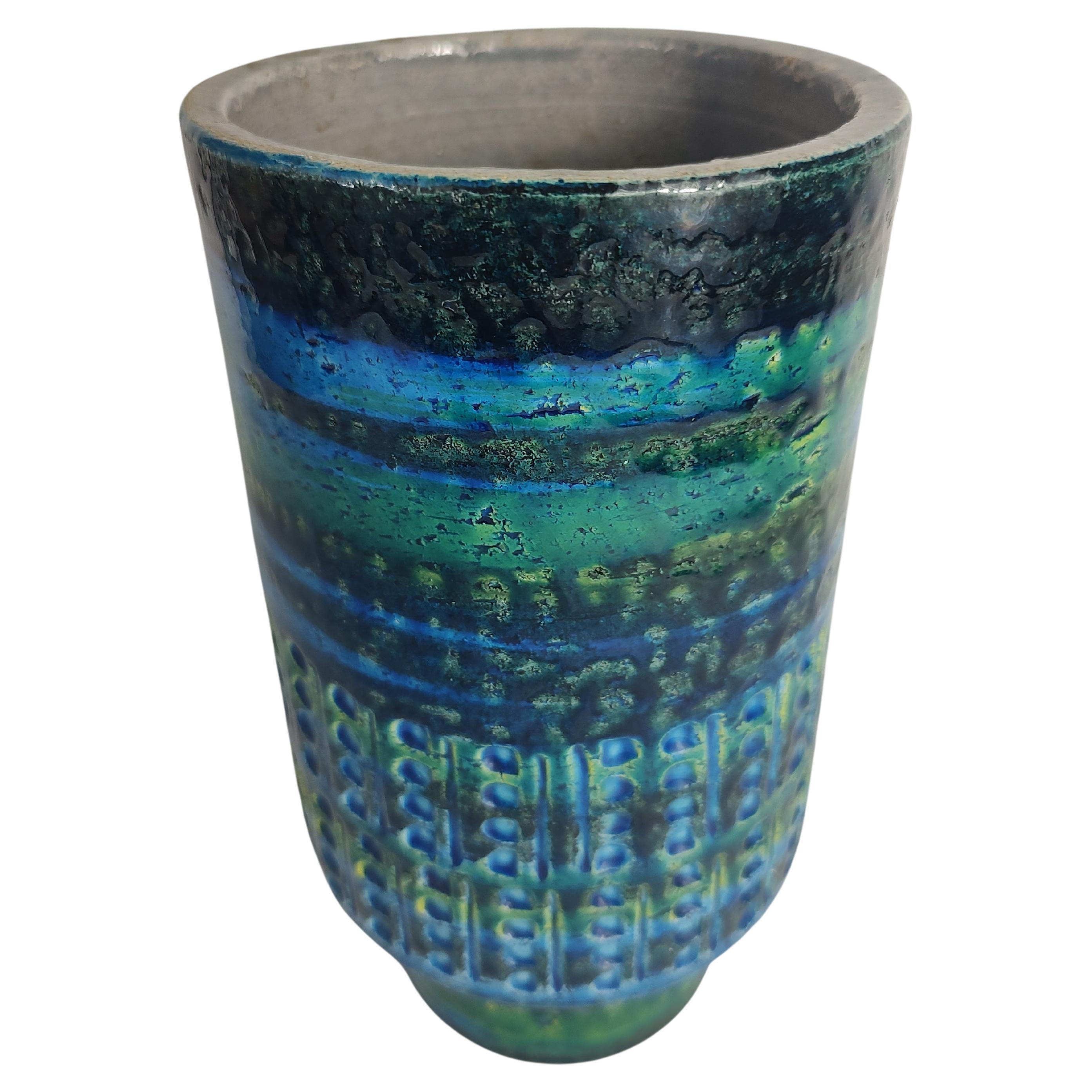 Fabulous cylindrical vase in Rimini Blue by Aldo Londi and Bitossi. Deep impressions surround the vase with a serene mix of blues and green. In excellent vintage condition with no visible chips or cracks. Vase has a set back pedestal like base.