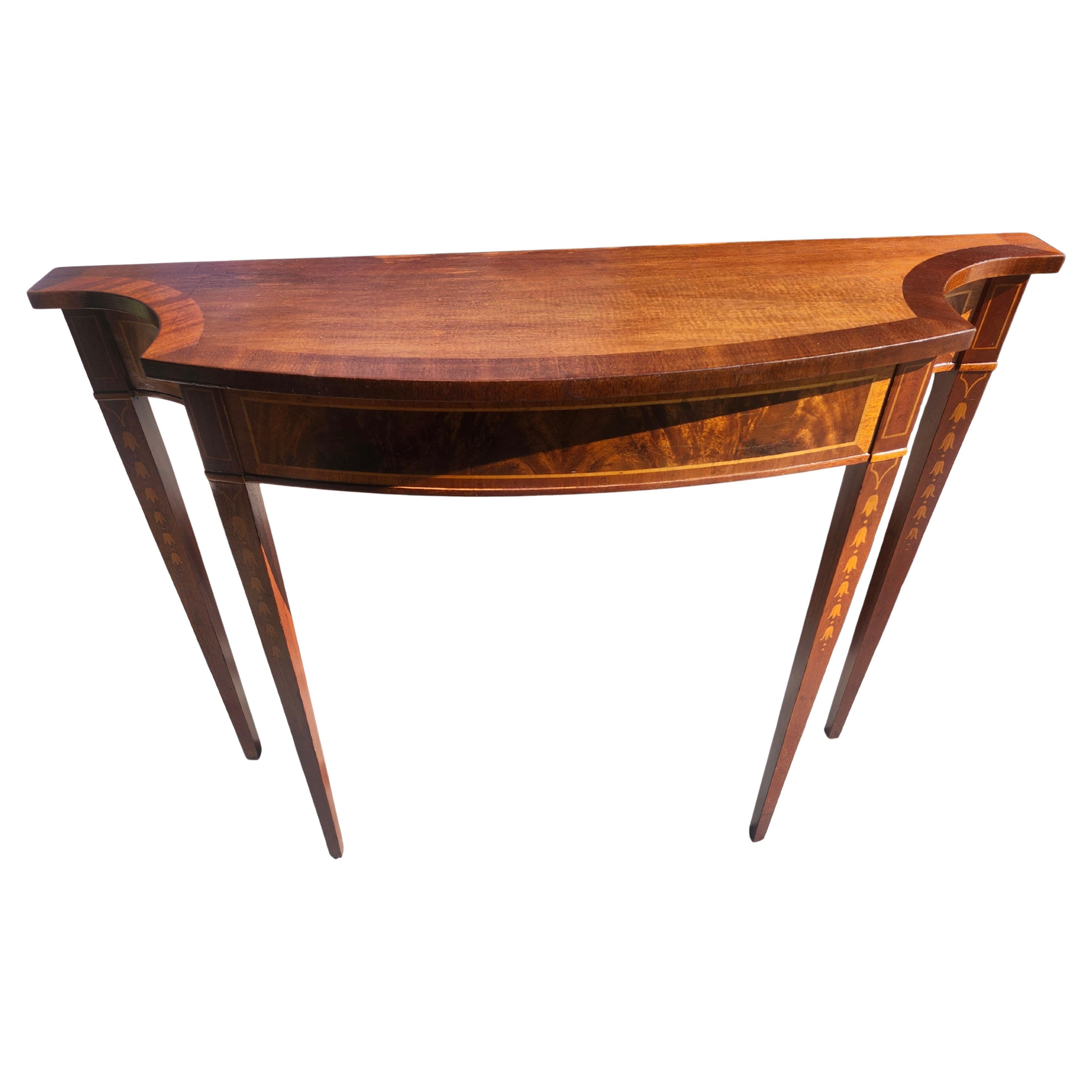 Sencilla y muy elegante consola demi lune de caoba con incrustaciones de bandas y flores de campana de marquetería en las patas. Mesa estilo Adams de los años 20 por Wellington Hall Ltd. Y está en excelente estado antiguo con un ligero