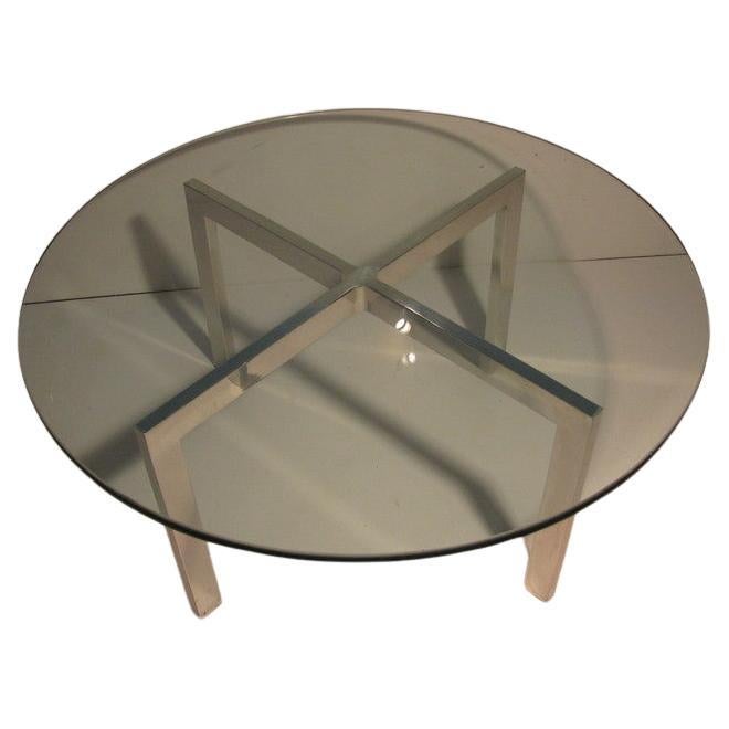 Polished aluminum cocktail table with cross X-form base, which is well executed. Dimensional heavy and 3/4 inch thick round glass top is original to the table. In excellent vintage condition with minimal wear. 