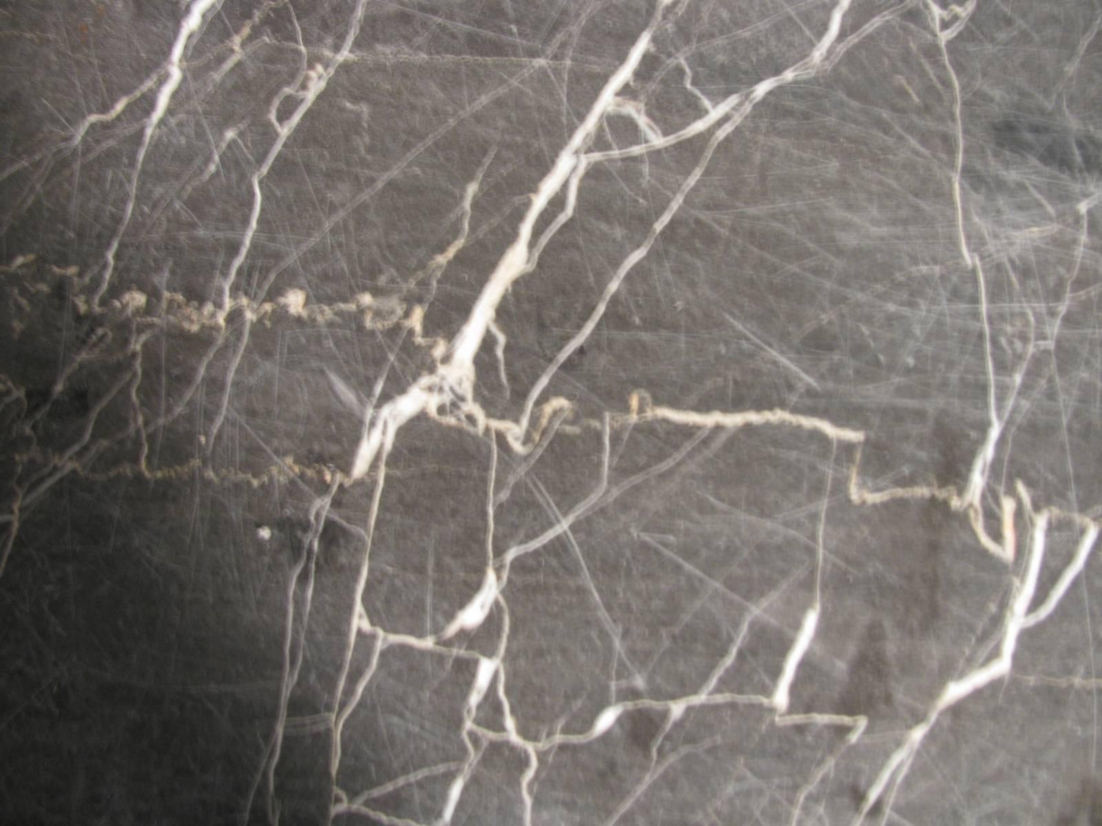 Heavily veined dark grey marble 1 inch thick which sits atop a cast iron base in the form of dolphins. Base and top are not connected, the base has wide flanges which support the marble. We have used outdoor Velcro with great satisfaction in the