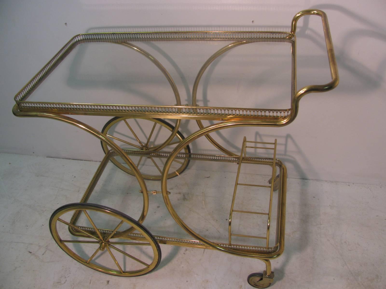 Sculptural brass with a pierced apron surrounding two shelves and a triple bottle holder. Large wheels with rubber tires for smooth gliding. Top shelf height is 26.5, shelf is 15.5 x 27.25.
