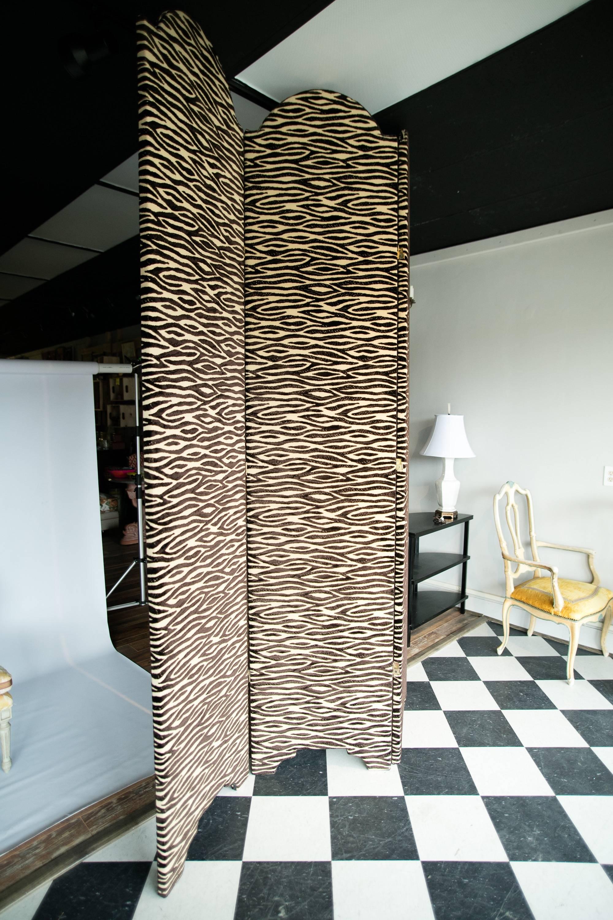 A contemporary upholstered screen from Baker Furniture. The screen is upholstered in a zebra-print black-and-tan cut velvet. The panels are arched on the top and have ogee-style legs. The panels are outlined on one side with bronze-colored nail head
