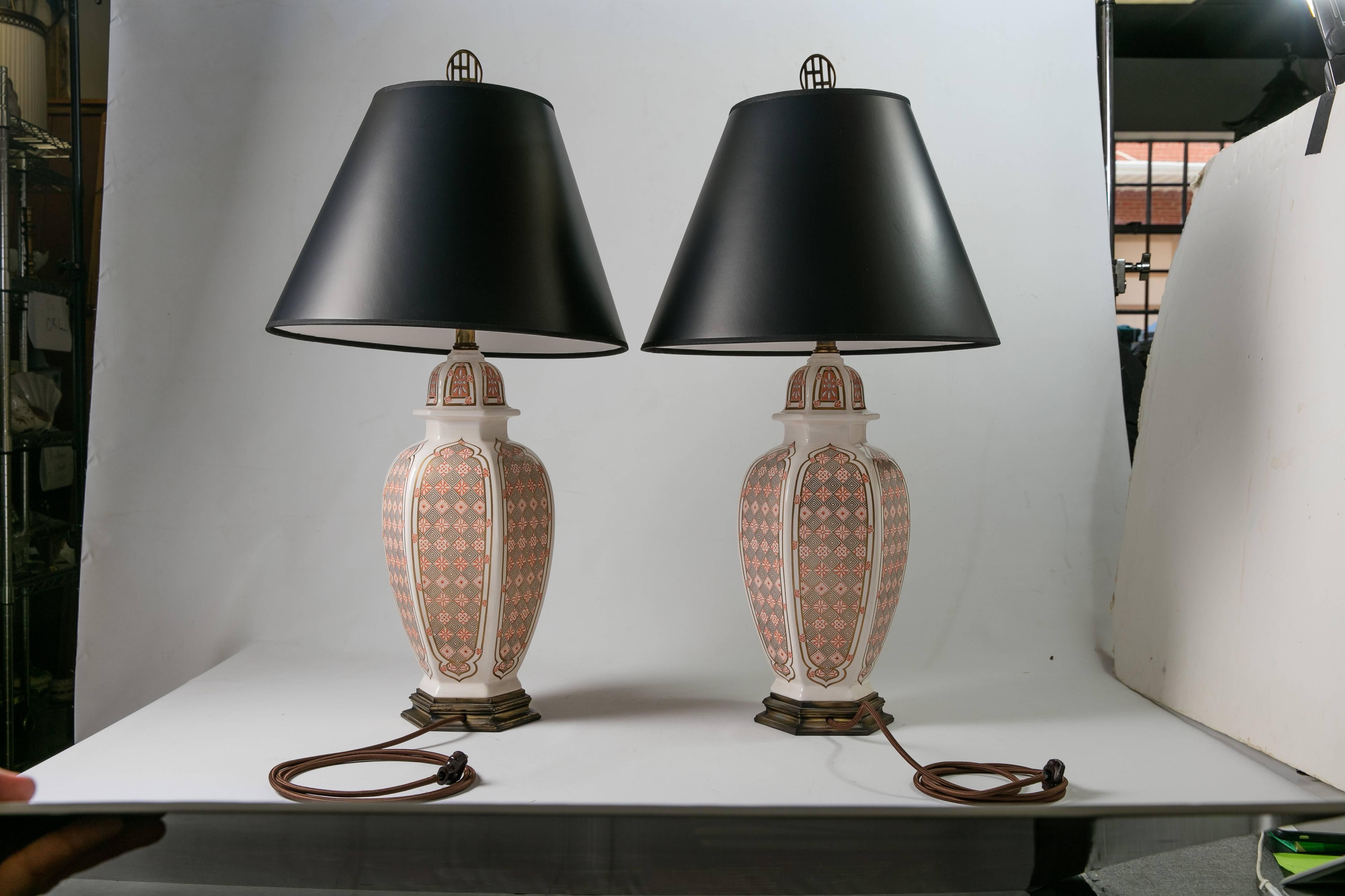 Pair of 1960s ceramic table lamps with a graphic Gothic-style print in orange and gold. The lamps feature a brass-colored metal bases and black paper shades. Newly wired with silk cords; 60W-max bulb per lamp. Shades, 9