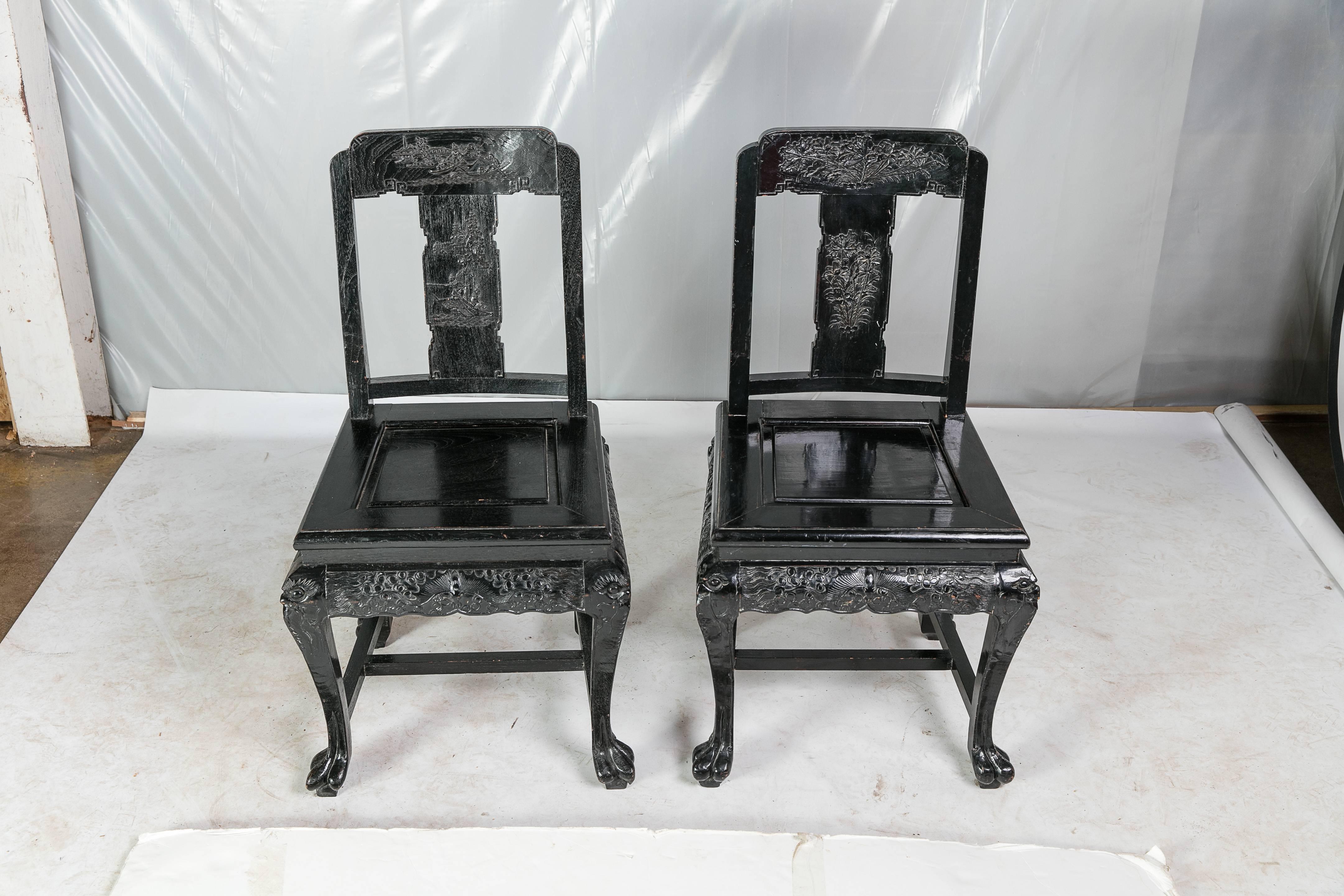 A beautiful pair of carved Chinese wood hall chairs by George Zee of Hong Kong. The chairs are circa 1950s and feature a black-painted finish. Each chair has heavily carved legs, skirt, and back. See photos for more detail on carvings. The back of