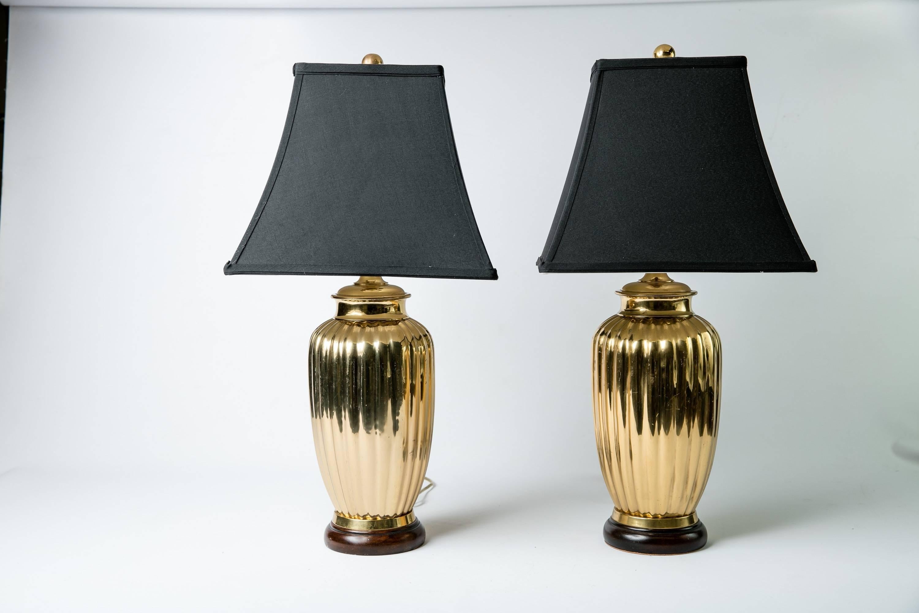 Pair of Deco-style heavy brass torpedo shaped table lamps with fluting and wood bases. The lamps have square corner bell-shaped black faux-silk shades. Newly wired and working; each lamp takes a 60W-max bulb. Measures: Shades, 7" diameter top x