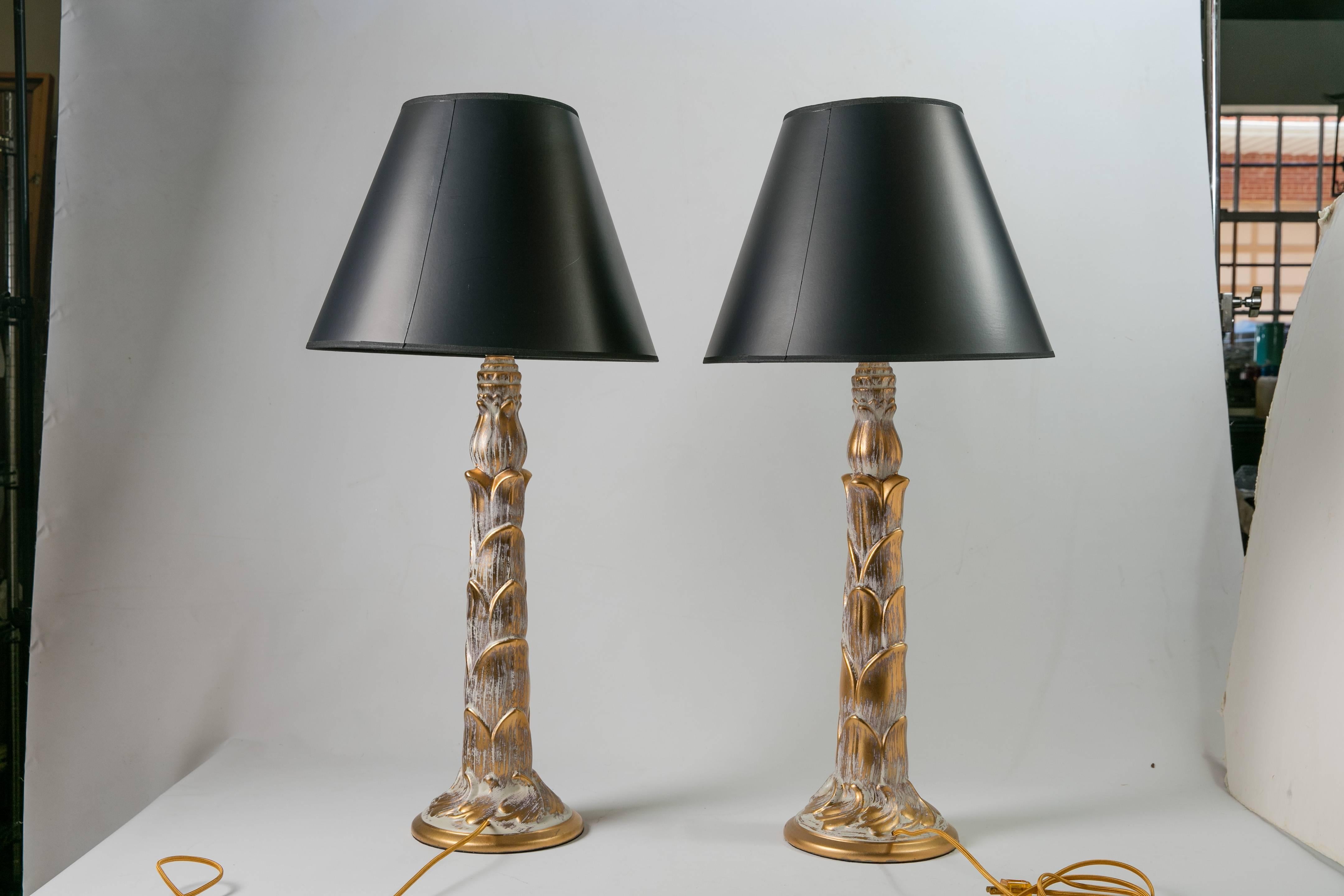 A pair of 1950s Hollywood Regency-style ceramic lamps with a white/grey wash and gilt highlights in the manner of James Mont. The lamps' shape is modeled on the trunk of a palm tree. Each lamp is newly wired with gold silk cords. Each lamp requires