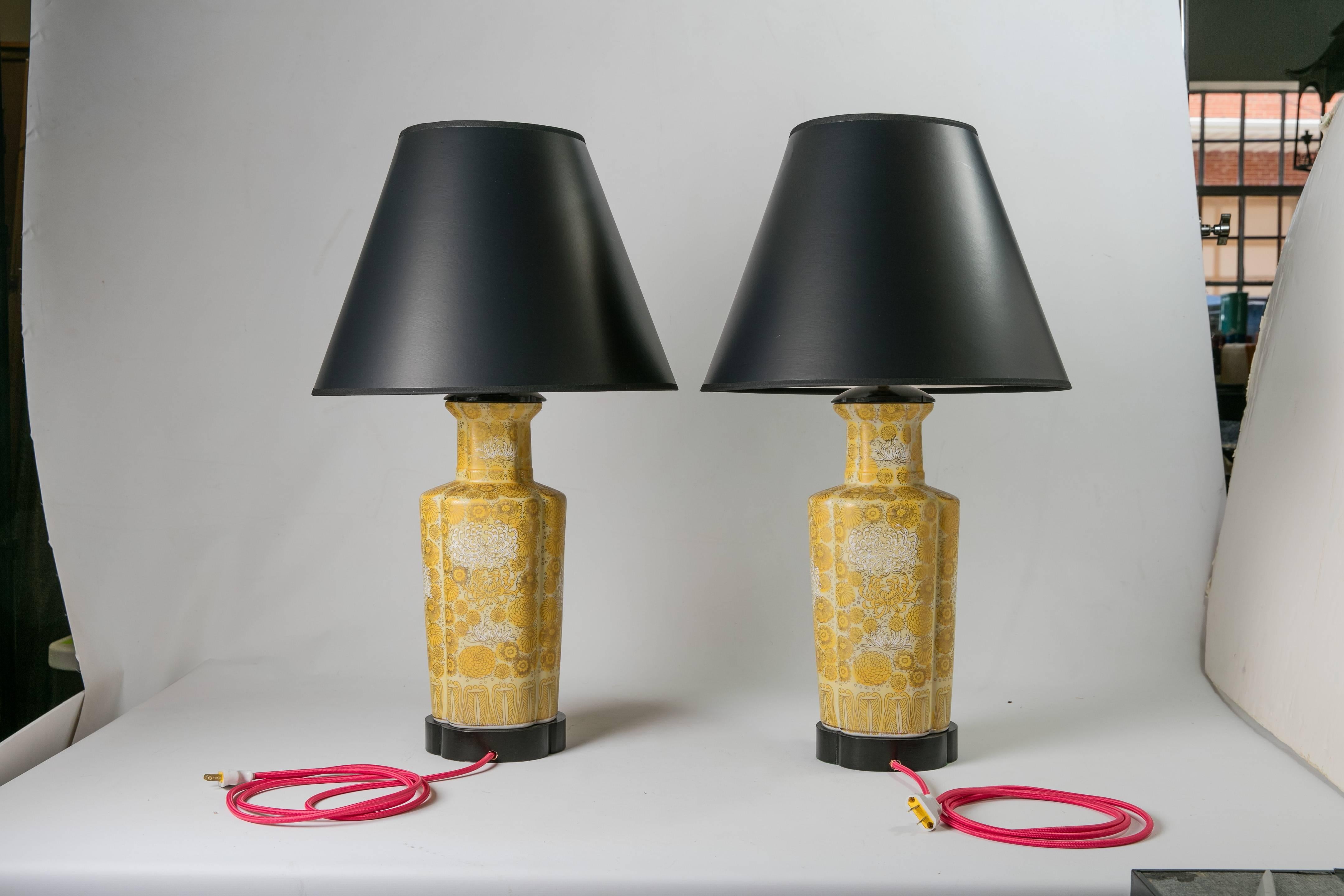 Pair of 1960s white-and-yellow ceramic lamps decorated with Imari-style yellow, white, and gold flowers. The lamps have black-painted wood bases and new black hardback paper shades. Newly wired with pink silk cords; 60W-max bulbs. Shades, 8