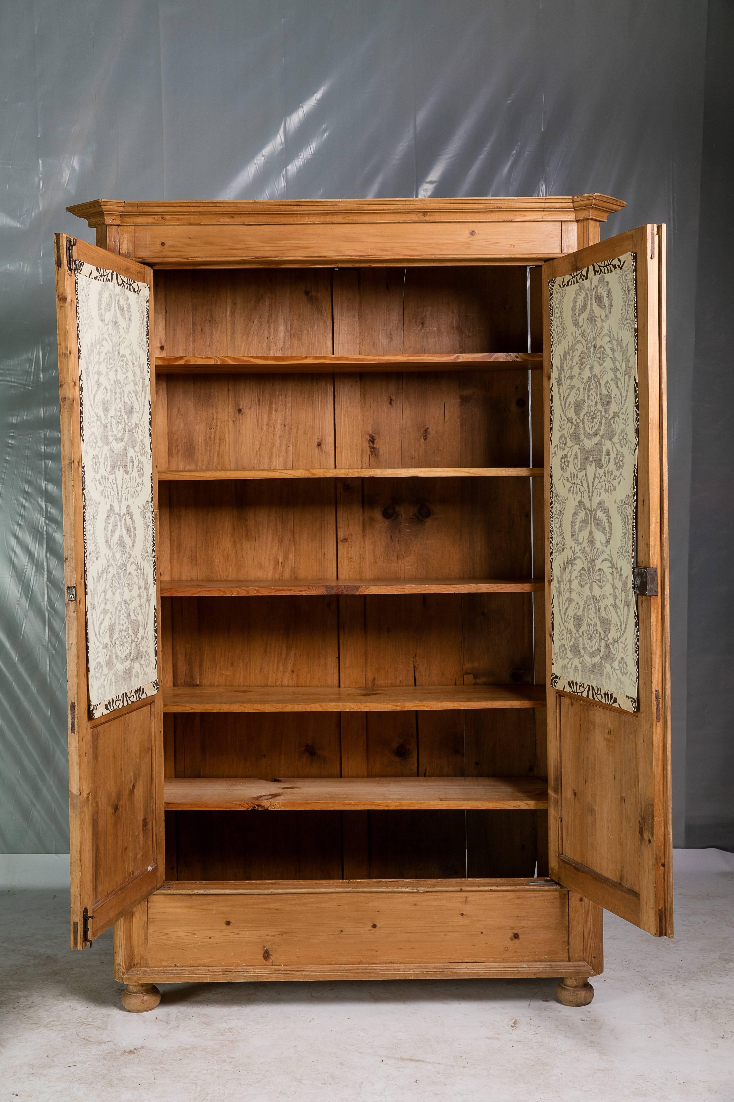 Mid-19th century pine armoire with paneled glass doors and five pine shelves. The shelves are a recent addition and rest on wood brackets that have been fixed in place for added stability. The glass portion of the doors have been covered from the