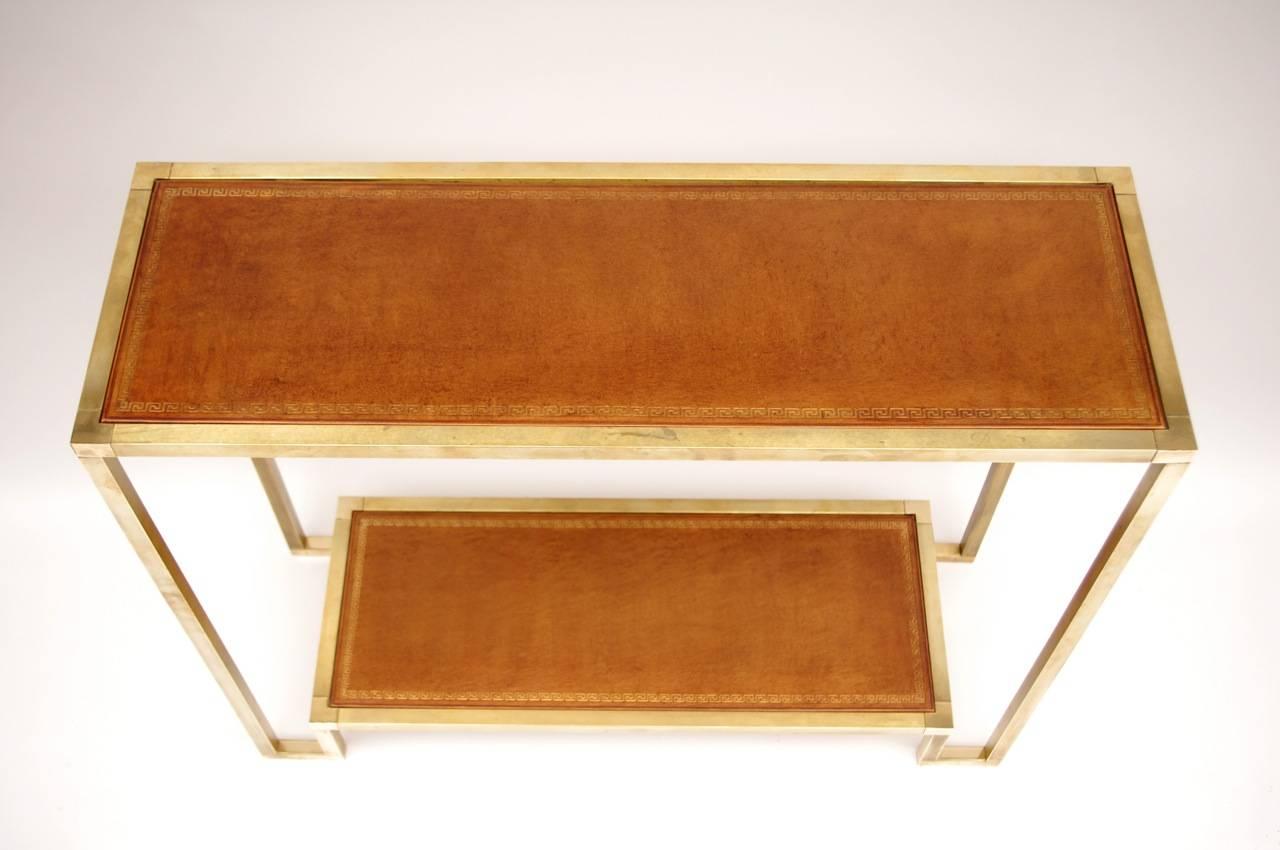 Gilt brass console with two trays covered by brown leather highlighted with gold.
Work made circa 1970.