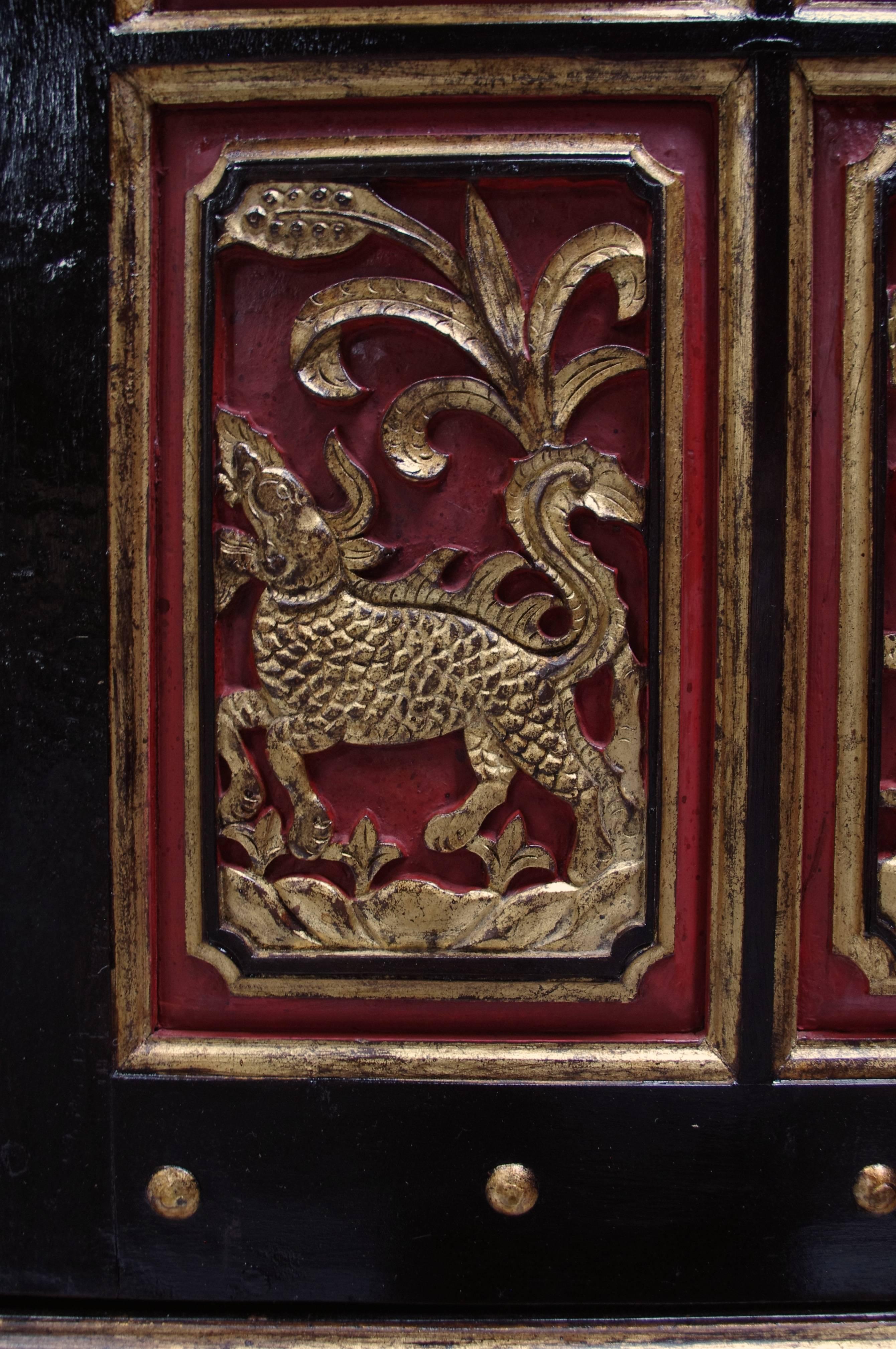 Indo-Dutch work.
Standing on four claws on bowl feet.
Red and black lacquer with gilt highlights.
Opening on two doors and two drawers.
Decorated with sculpted animals and foliage frieze,
1900 period.