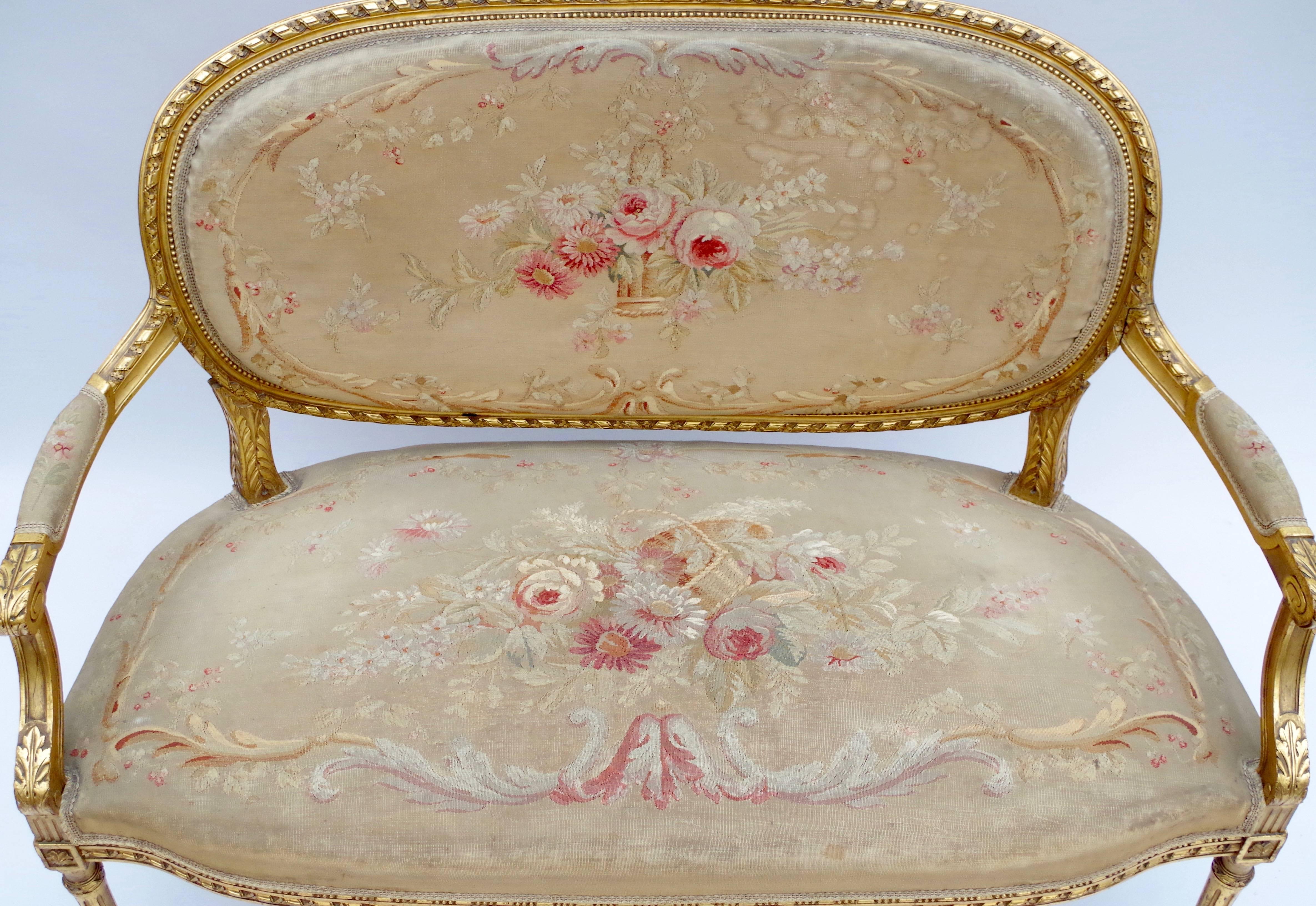 - Set of four armchairs and small sofa
- Carved and molded giltwood
- Decoration of twisted ribbons, flowers, acanthus leaves and rosette
- Fluted tapering legs
- Original Aubusson tapestry fabric
- Louis XVI style
- circa