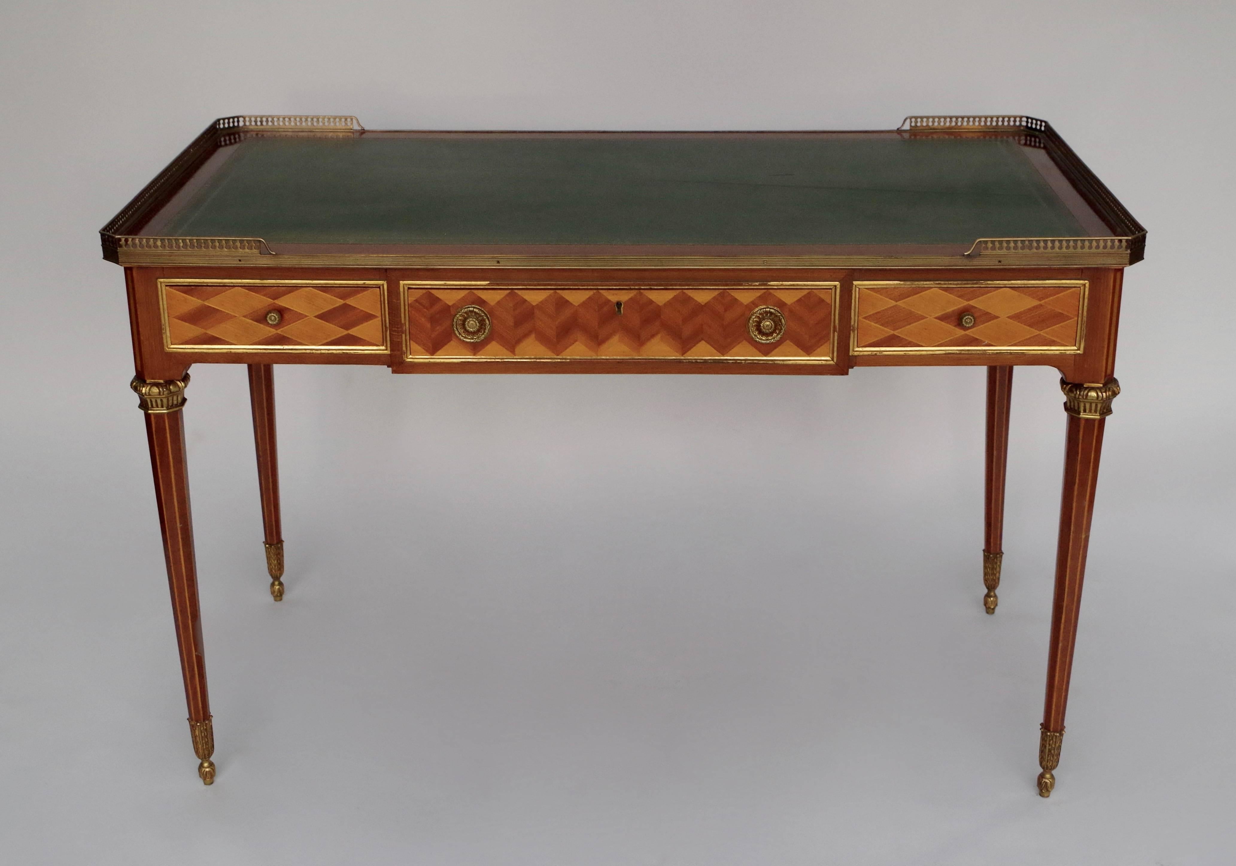 Louis XVI style salon table / flat desk in mahogany decorated with geometric marquetry in mahogany and satinwood with rafters patterns on the central drawers and diamonds patterns on the side drawers, framed with gilt wood molding.
Top in green