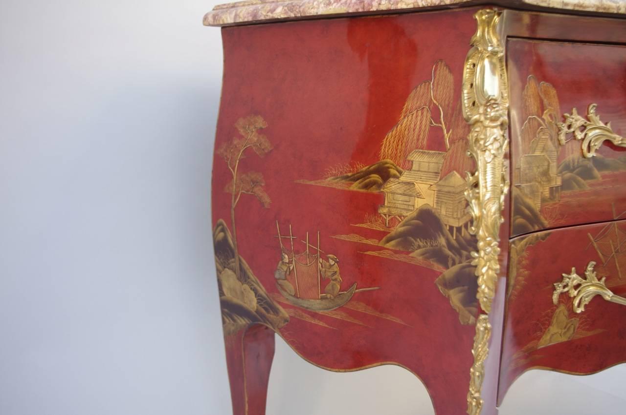Louis XV style sauteuse commode in red background lacquered wood and gold highlights with Chinese decor. Bulged form, opening by two drawers without crosspiece. Lacquered wood decor figuring fishing scenes in water landscapes. Gilt bronze decorative