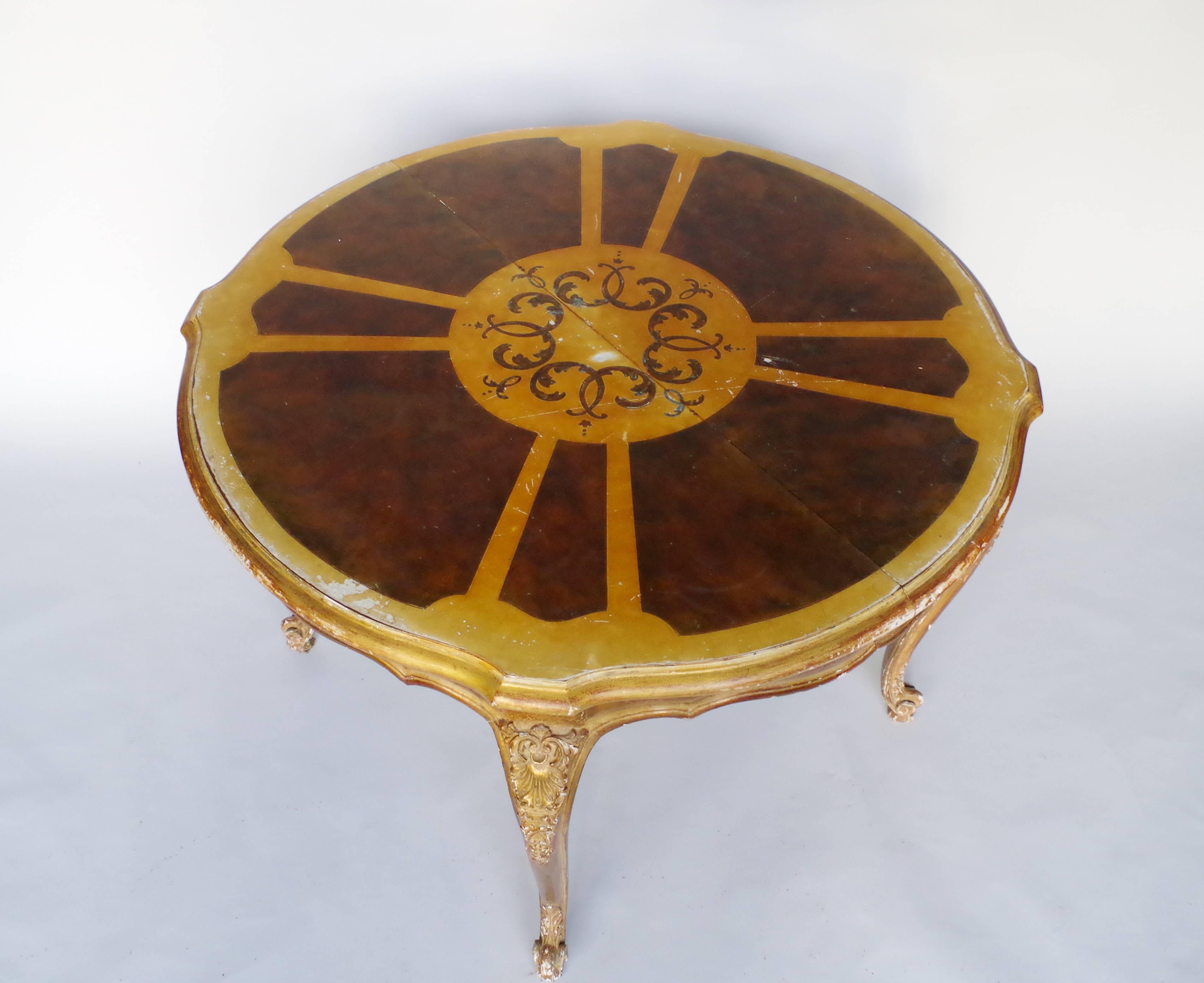 Louis XV style giltwood round table with extensions. It rests on four curved legs ending in windings. The belt and the legs are decorated with squares, shells and acanthus leaves. The top is lacquered and decorated with a central round medallion