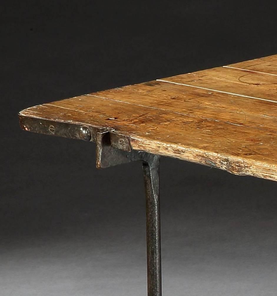 Table with architectural pair of ironwork trestles
and well patinated, double-sided, metal bound pine top.