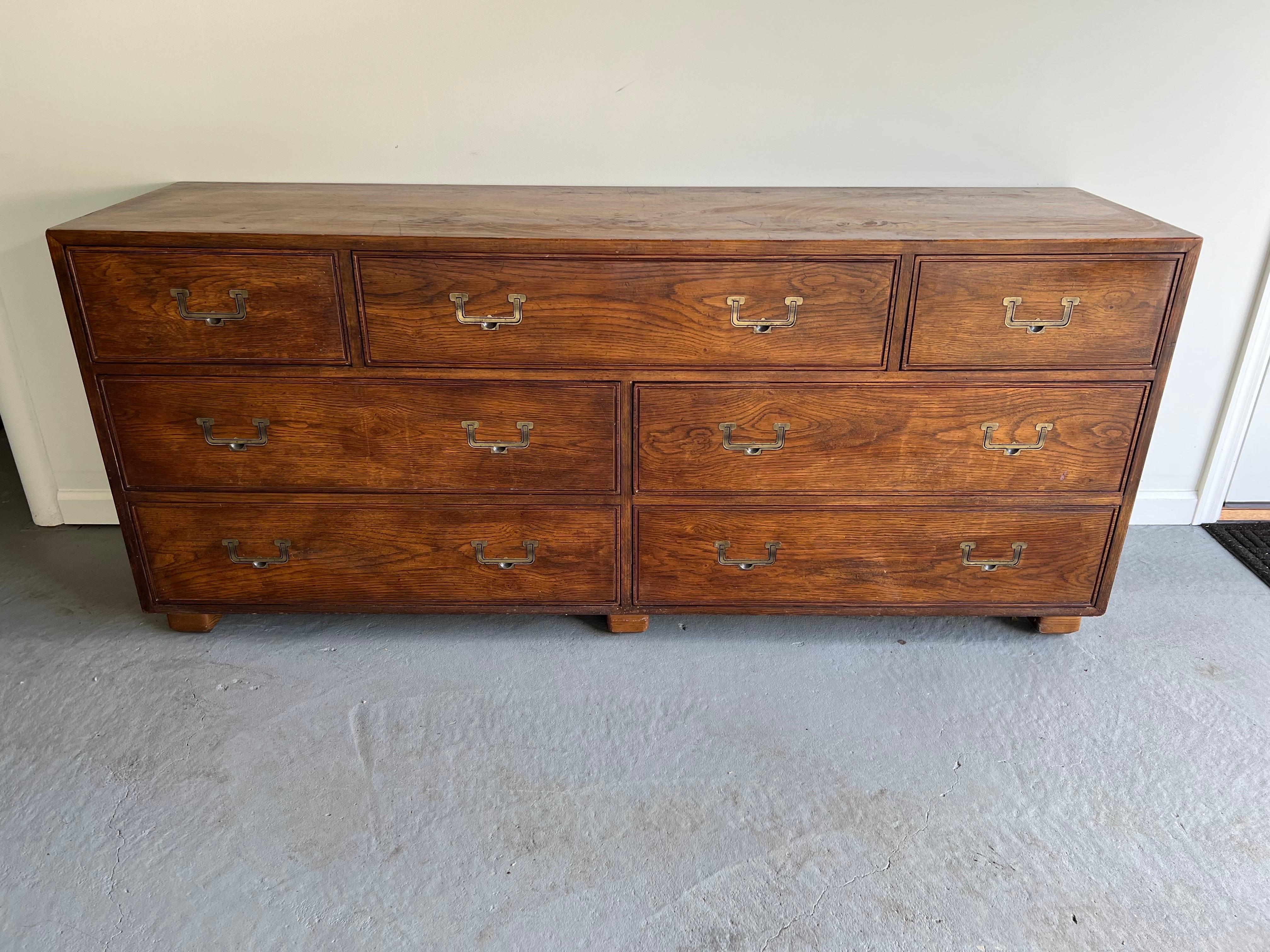 Henredon Artefacts Campaign style dresser. This seven drawer beauty has solid wooden (oak) construction with solid antique brass handles. It has a classic timeless style with its minimalist recessed brass hardware . There are drawer dividers in the
