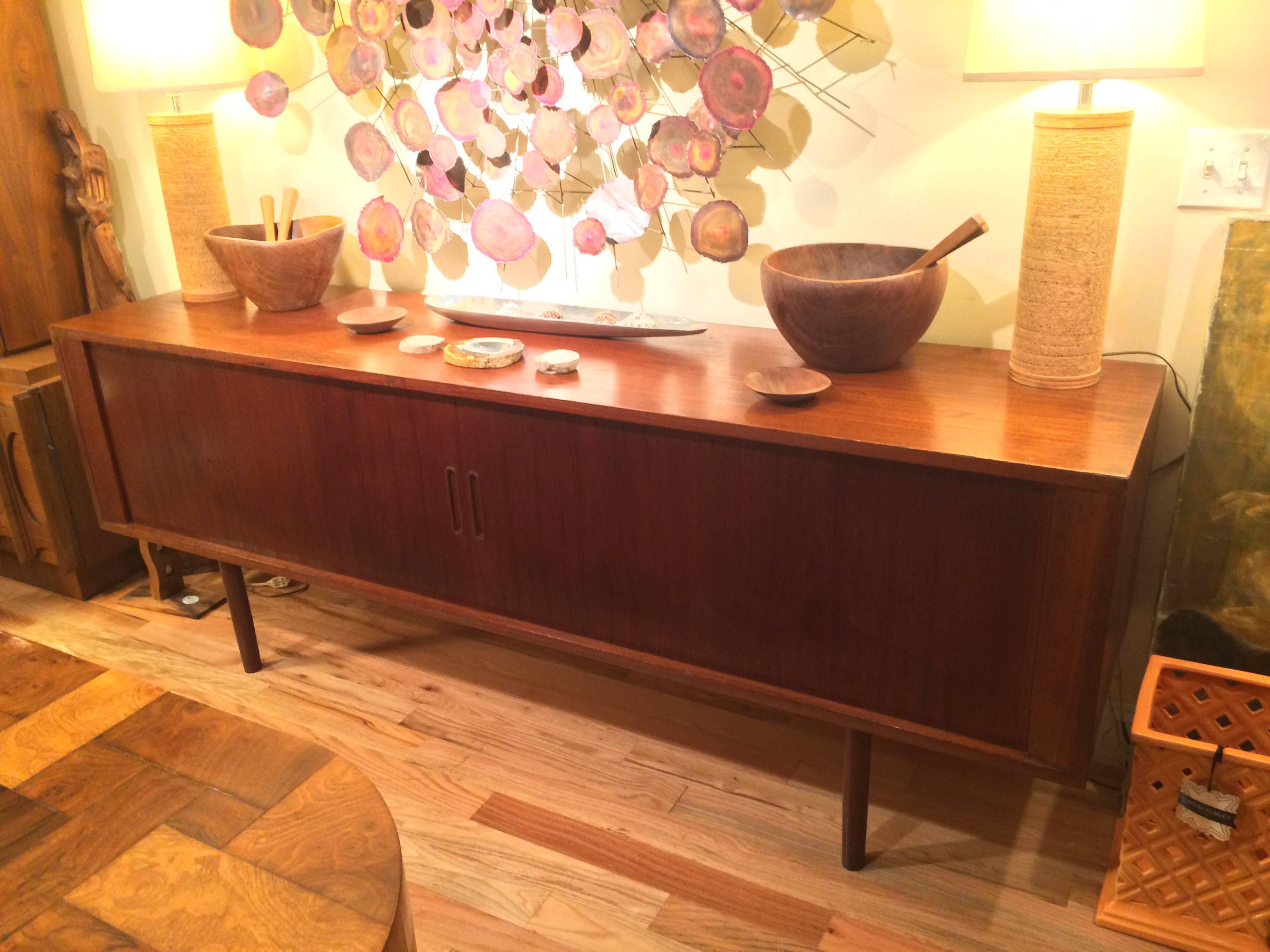Danish Modern teak tambour door credenza. Three center drawers and two-shelves are revealed when the tambour doors retract open. The top drawer is felt lined and has racks for silverware. The item is stamped on the back with the Danish makers mark