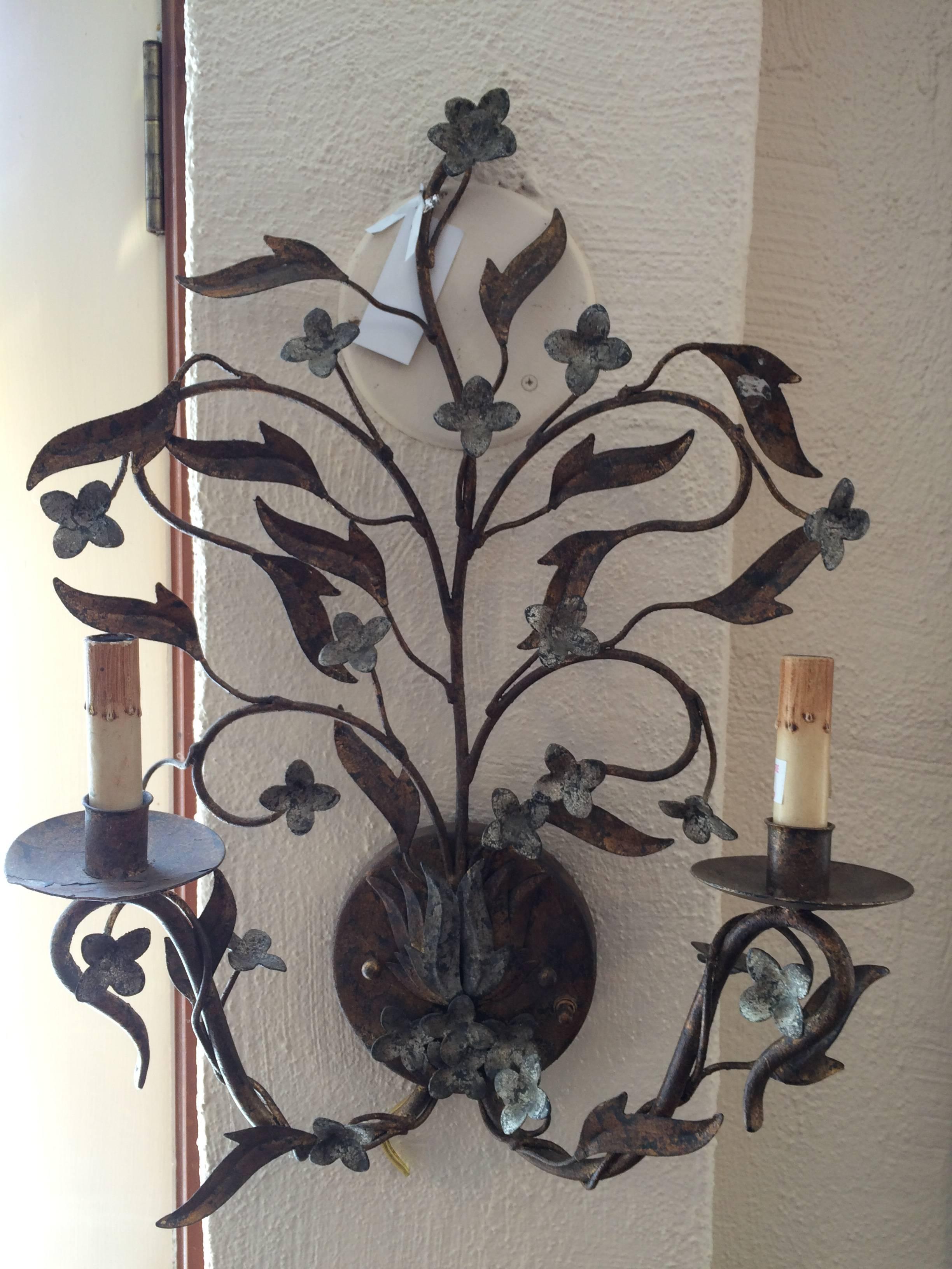 Floral double armed iron sconce. Gilded with gold and silver this delicate piece of sculpture would be a beautiful illuminating addition to any wall. The floral highlighted accents are closer to a light gray than a verdigris or a blue gray. see