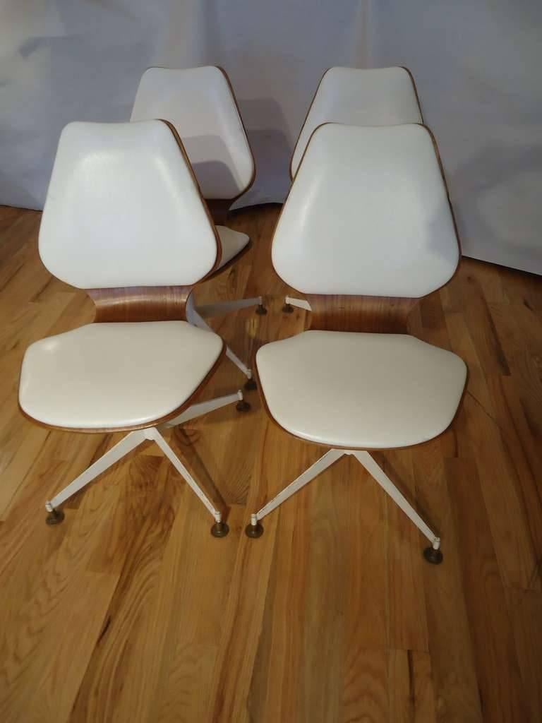 Set of four Mid -Century Modern teak bentwood swivel chairs. These classic  chairs with original white vinyl upholstery swivel showing the beauty of both front and back sides. One chair missing the original brass glider/foot.
