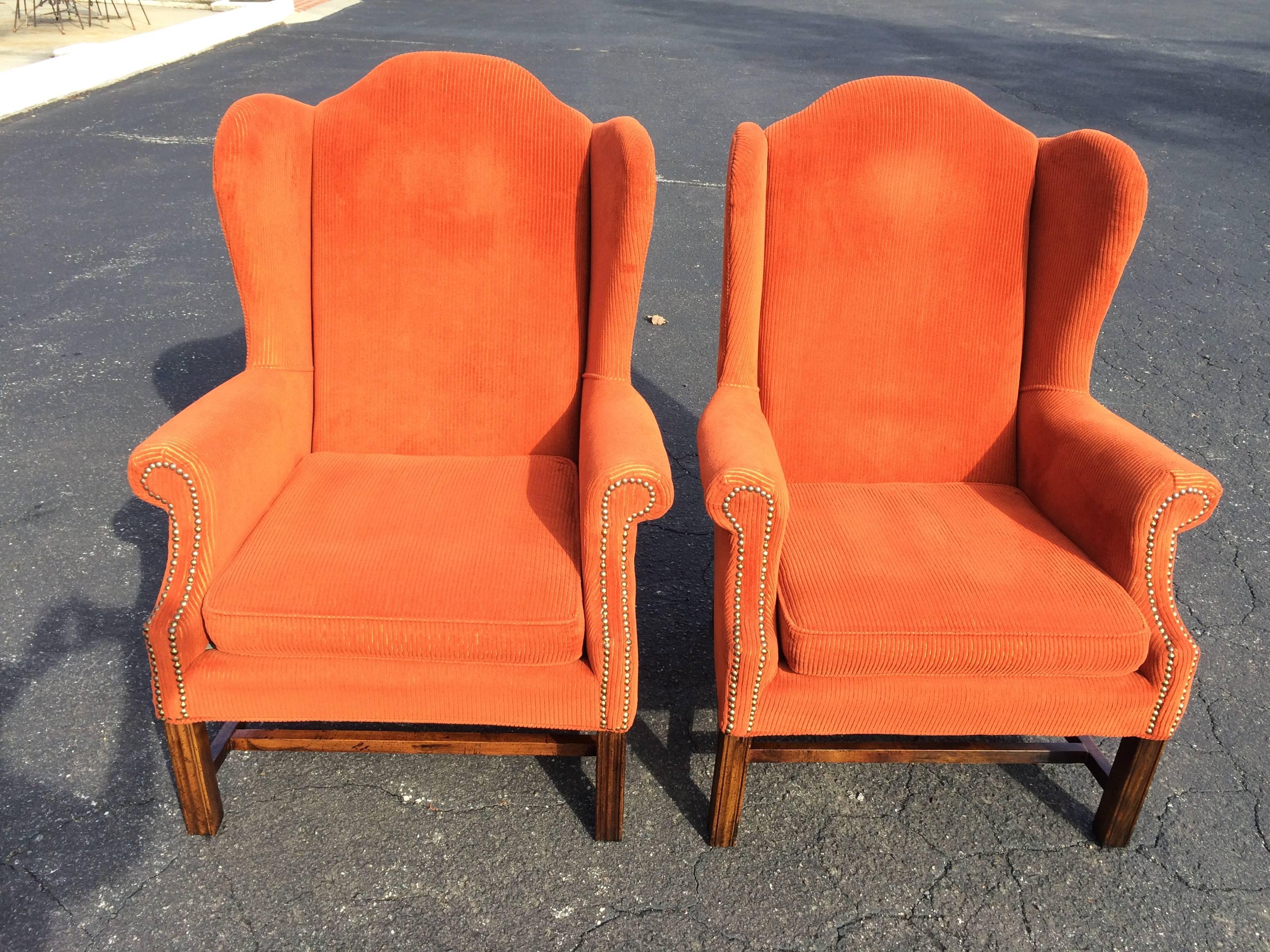 Pair of orange corduroy wing back chairs. Traditional in style but fun in color. This pair of chairs has brass nail head trim and sturdy wooden base. Put these in front of your fireplace and relax.
 