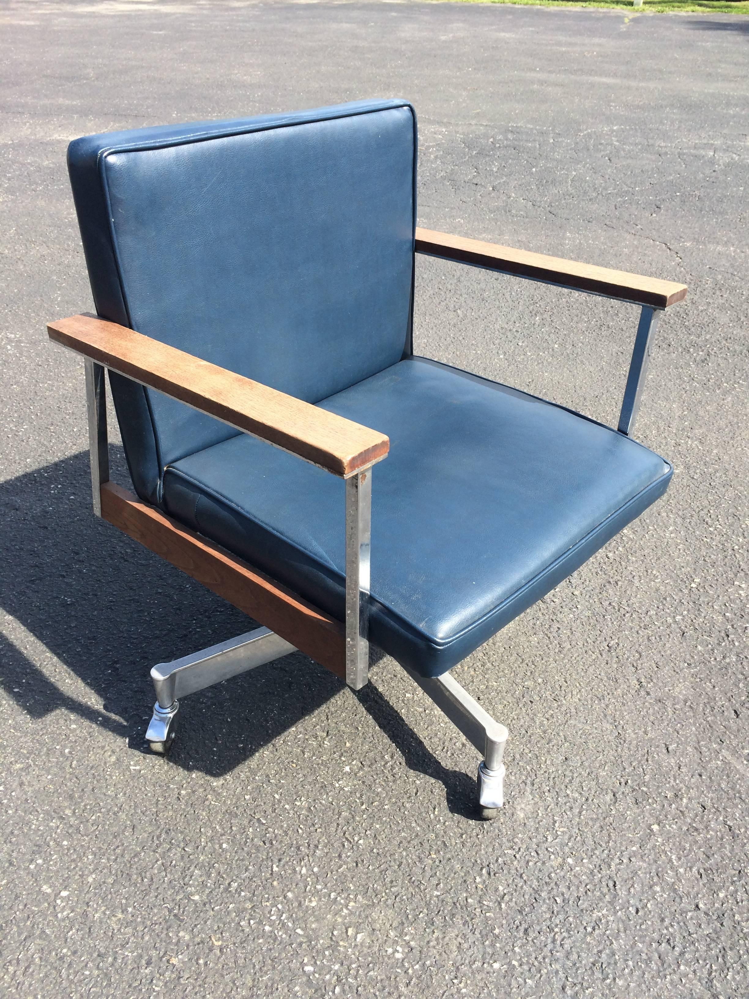 Mid-Century office swivel chair on casters. With walnut arms and side accents this  navy blue vinyl chair is a classic. Chrome casters and base give this chair a nice contrast .This chairs swivels and is adjustable in height. It can also slightly