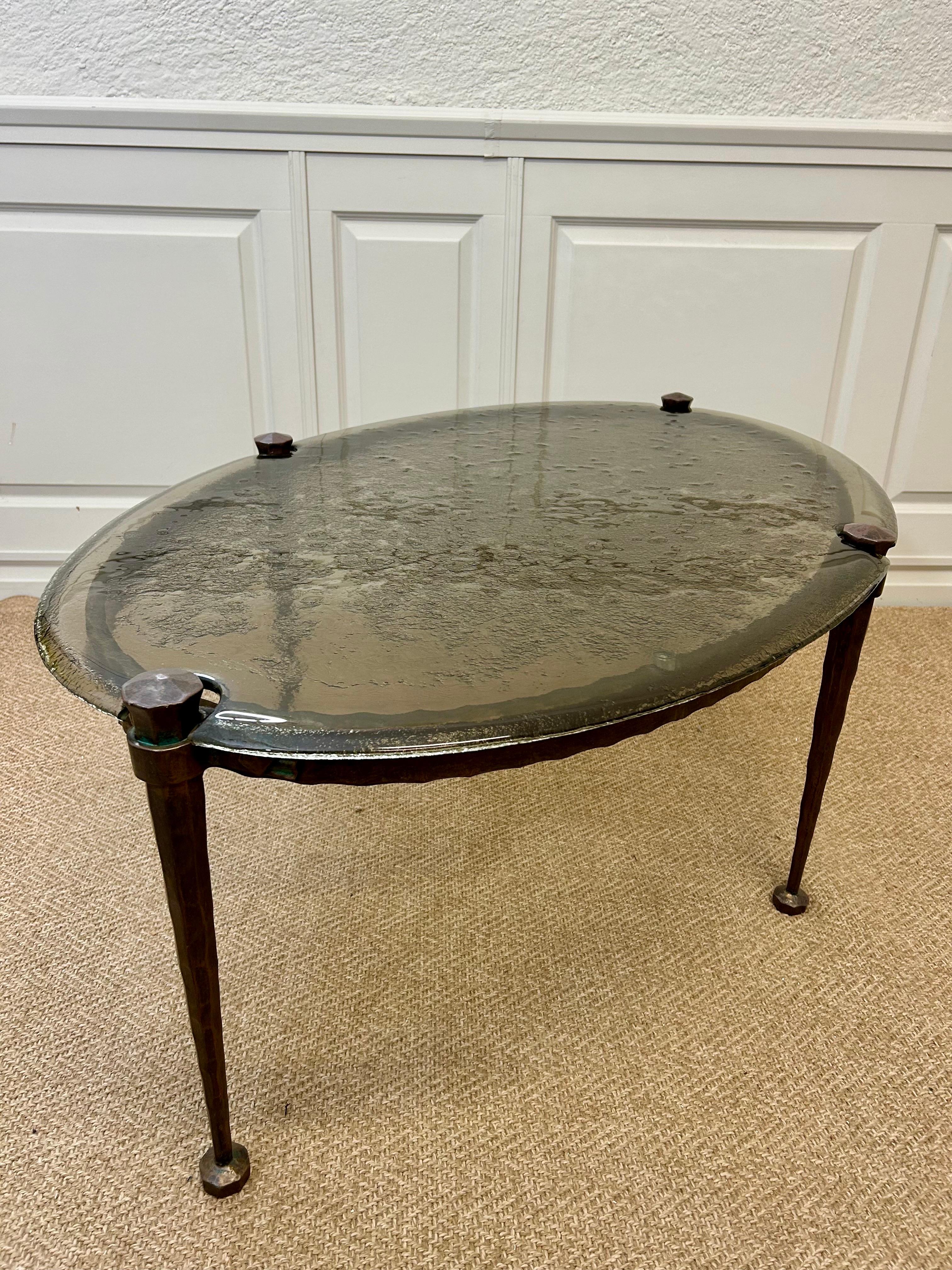 Avec son plateau en verre de cristal moulé à la main et son cadre en bronze magistralement forgé, cette table basse ovale du sculpteur et forgeron allemand Lothar Klute est un meuble plutôt substantiel mais élégant dans le style brutaliste.

Connu