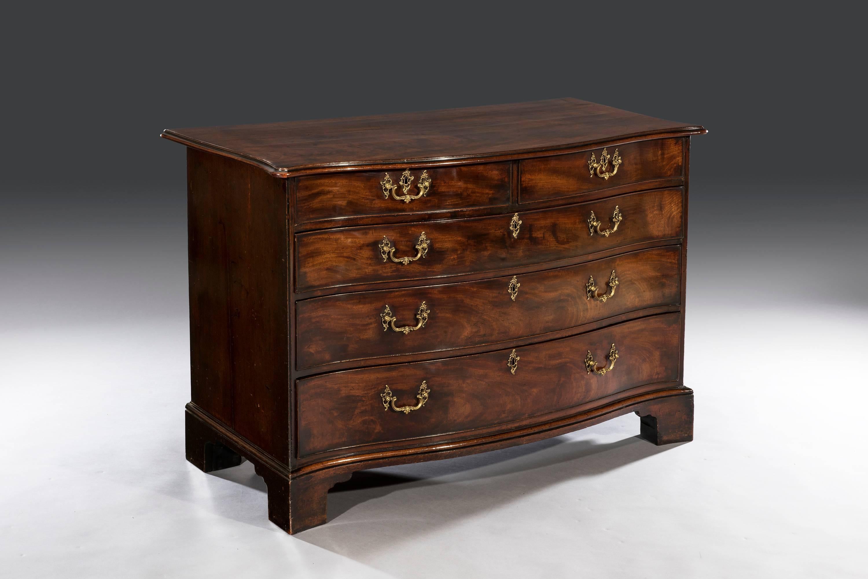 The serpentine shaped rectangular mahogany top with a thumb nail moulding sits above two short and three long graduated oak lined drawers. The commode has solid mahogany sides and tightly drawn canted angles. The highly figured mahogany drawer