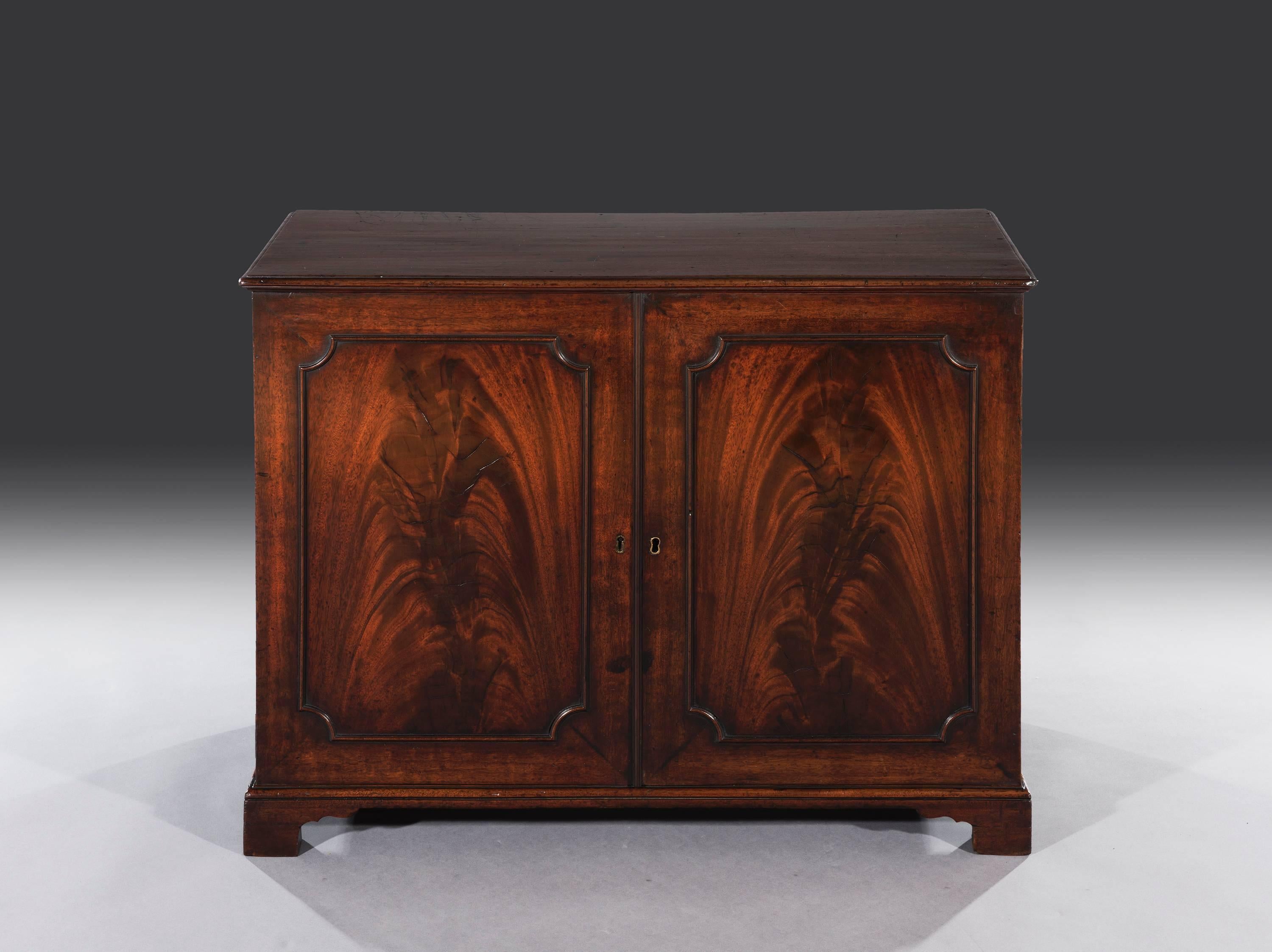 The cabinet is rare and unusual as it only stands two fee high. The mahogany moulded top sits above two flamed mahogany panelled doors which enclose a single adjustable shelf. The cabinet rests on a solid plinth moulding that sits on the four