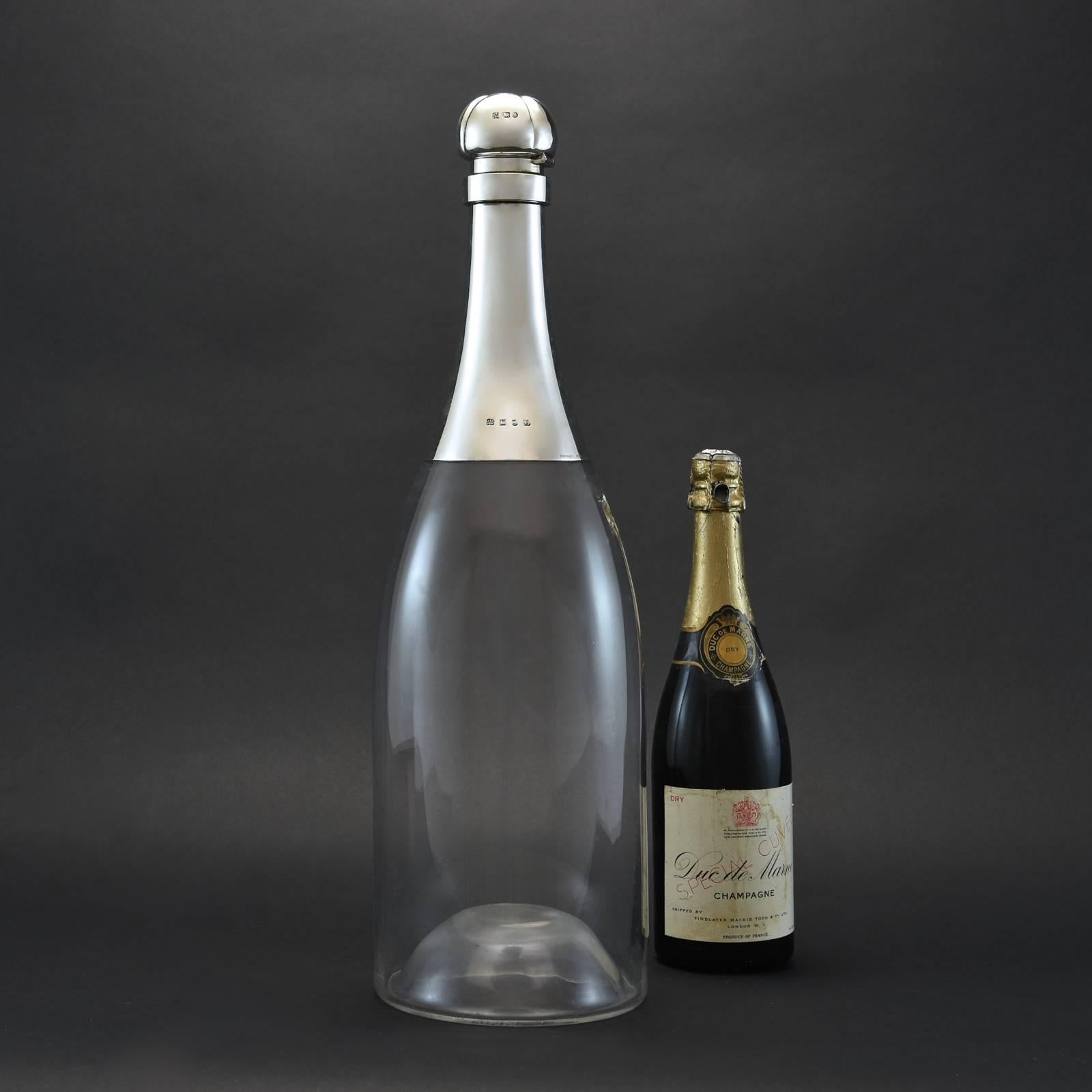 Extraordinary oversize decanter in the shape of a champagne bottle.
It has a capacity of just under 6 litres (thats more than 7 bottles of wine!). 
The Sterling silver neck and hinged stopper have hallmarks for the year 1892 and makers marks for
