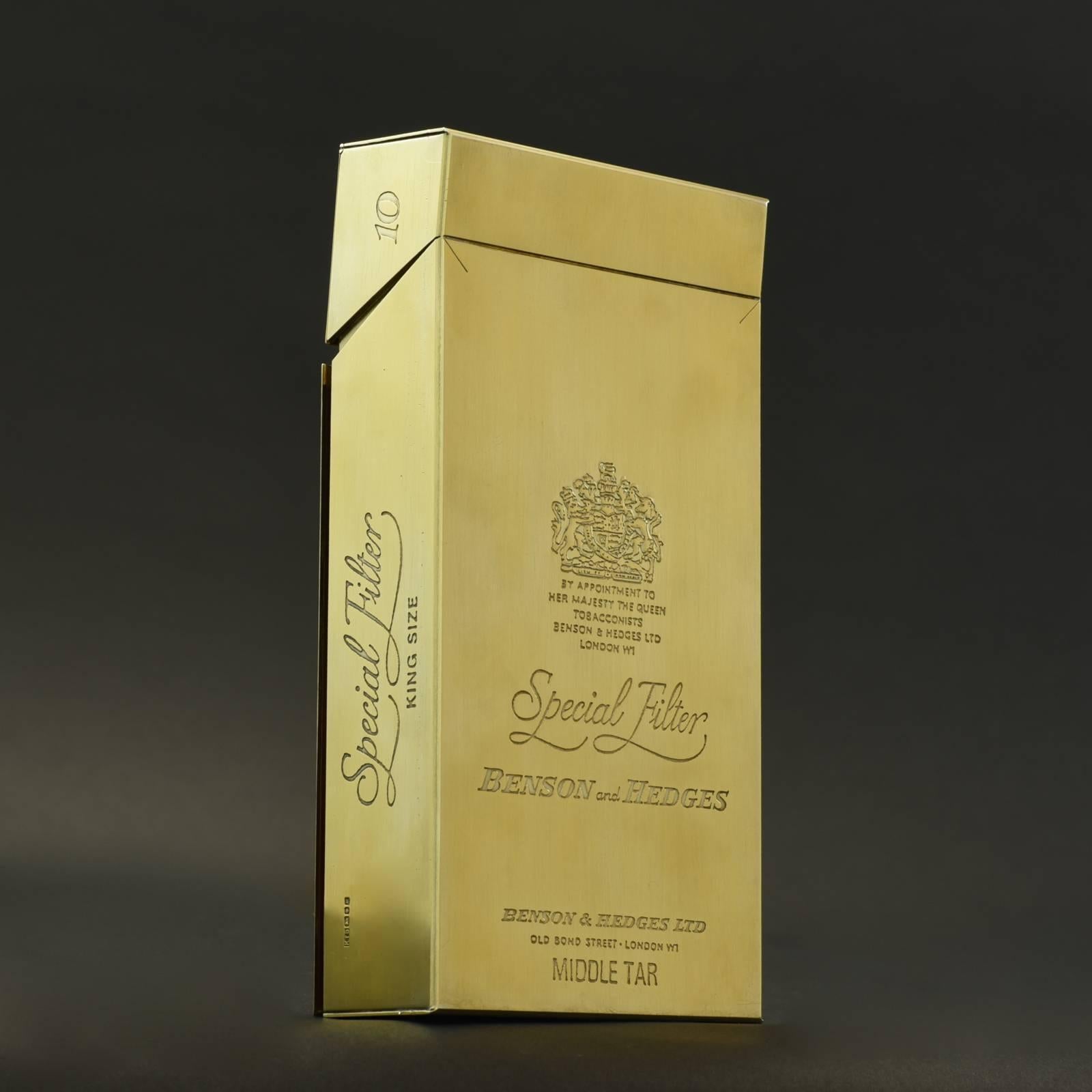 An extraordinary silver-gilt smokers compendium modelled as a Benson and Hedges cigarette packet by Karel Bartosik hallmarked, London, 1986. The box is a scaled up replica of a packet of ten cigarettes engraved and embossed with the logos and