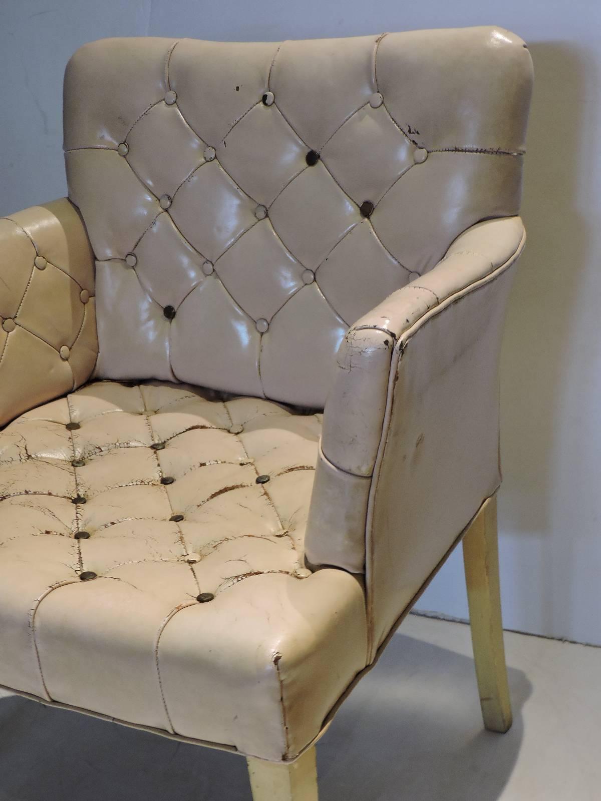 A great looking 1940s Regency worn pale pink leather button tufted chair with original cream white painted tapered legs and front brass casters. In the style of Tommi Parzinger / Grosfeld House.