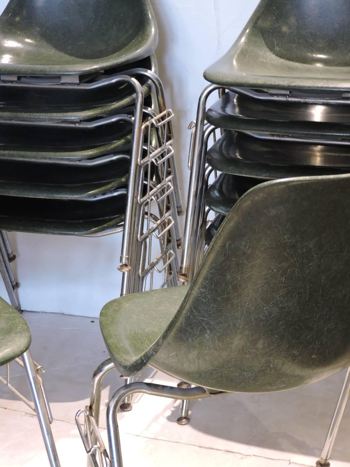 In the style of Charles & Ray Eames for Herman Miller - a group of 12 mid-20th century dark olive green fiberglass shell chairs with tubular steel stacking and locking framework. The dark olive green fiberglass has beautiful all-over exposed fiber