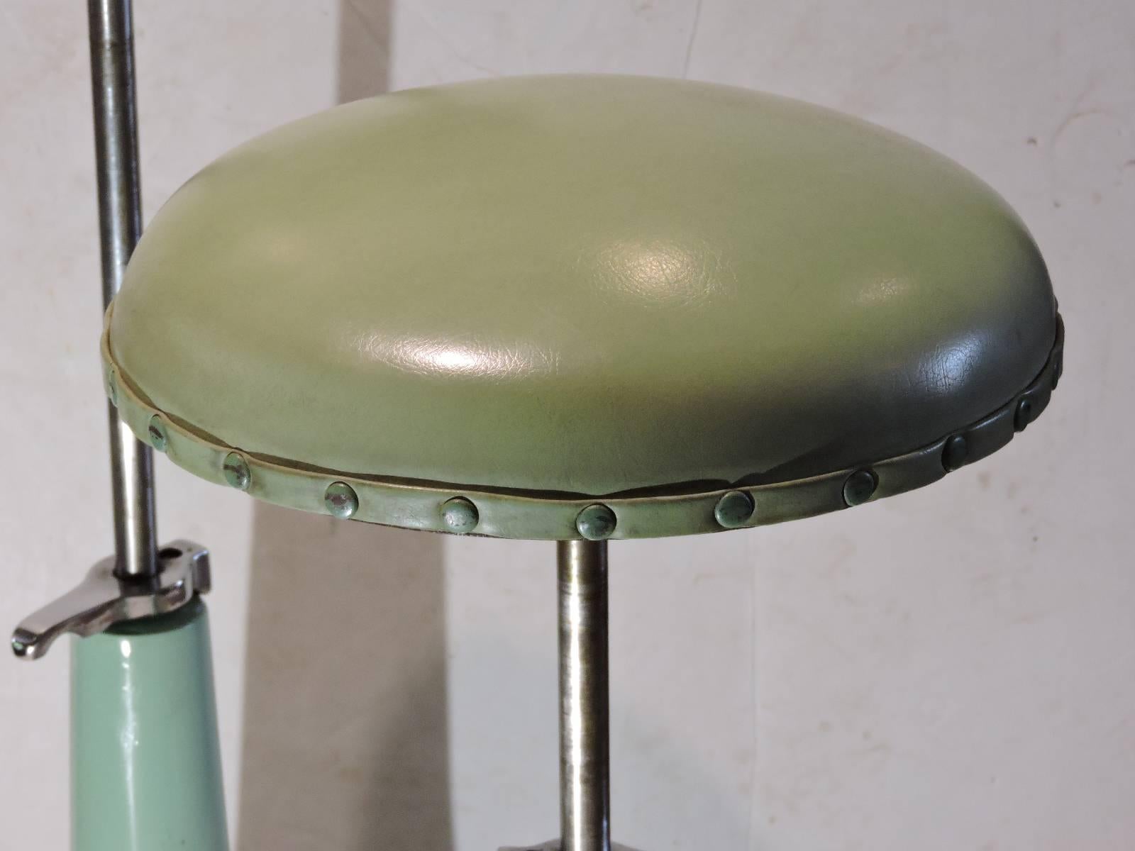 A great pair adjustable height Industrial optical swivel stools by Bausch and Lomb in all original stainless steel and pale mint sea foam green enamel painted steel. The pale olive green leather like vinyl upholstered seats with metal tacking are