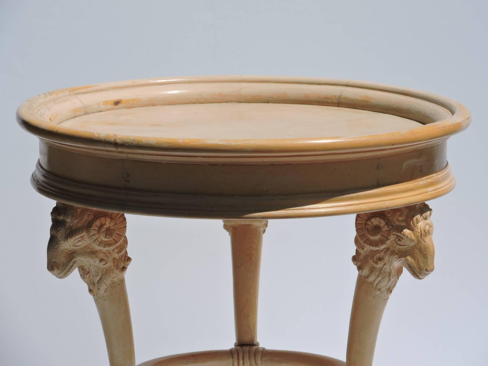 In the style of Grosfeld House, a mid 20th century Neoclassical style table in original white washed finish w/ three carved rams heads under apron of recessed circular top - legs ending in three hoof feet. Look at all pictures and read condition