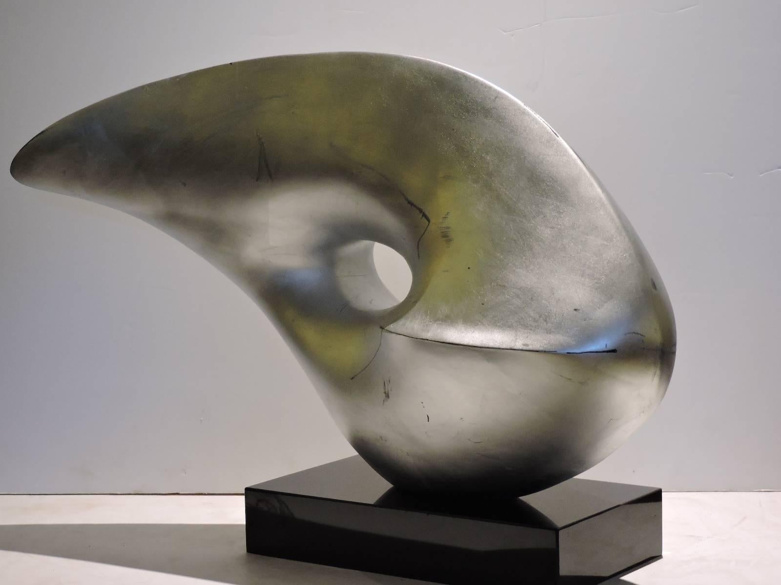 In the style of Barbara Hepworth, a large-scale modernist abstract silver leaf painted fiberglass resin sculpture bolt mounted on a polished rectangular black marble base. Pictures show a number of viewing perspectives from both sides and different
