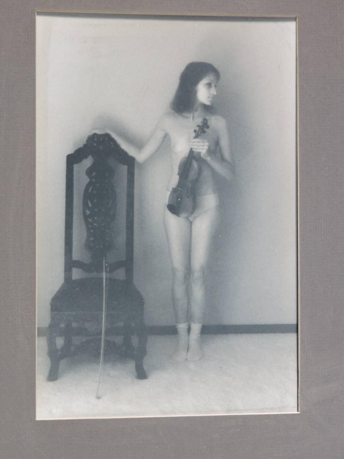 A sensual black and white to slightly sepia tone interior photographic image of a partially nude woman holding a violin, pencil signed dated and numbered by artist on right side of mat below image.
8/20 - E. Lelental, 1974.