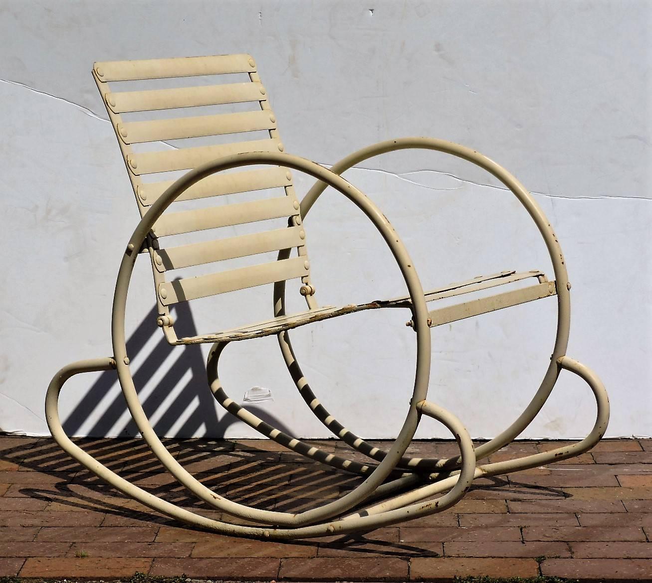 Streamlined American Art Deco slatted and riveted tubular steel  patio deck garden rocking chairs in old cream white painted surface. The chair with continuous sculptural large round hoop sides and horizontal slats is a very hard to find form rare