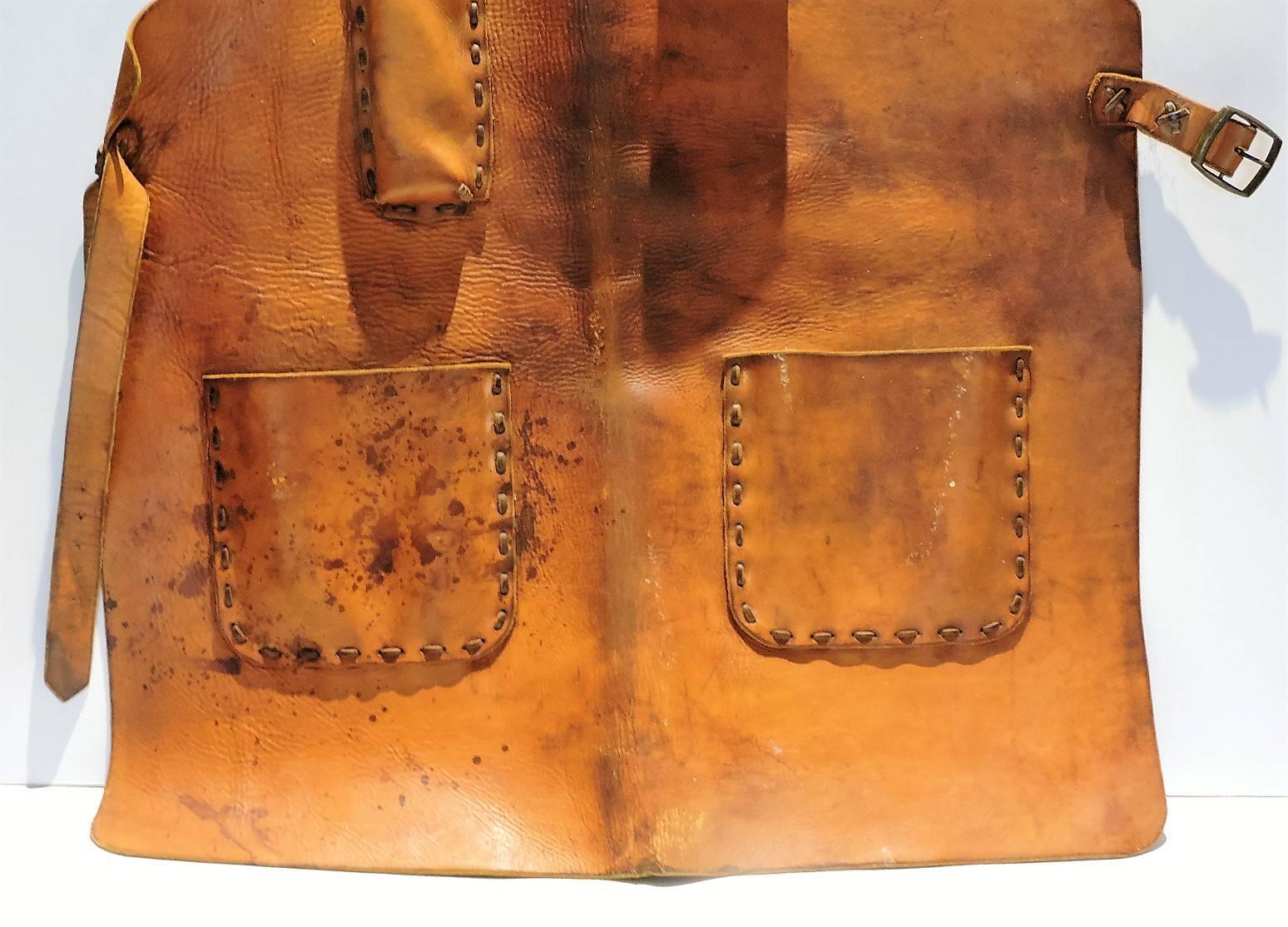Antique stitched leather apron with four raised pockets and belts at sides for Industrial blacksmith sculptor in beautifully age color patina to natural leather.