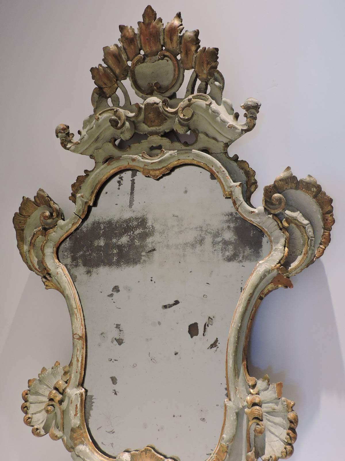 A very boldly carved antique Venetian Rococo mirror in older very pale soft gray to cream white painted surface with beautifully aged old gilding and scattered areas of loss to wood. The antique mirror glass with lots of oxidation and some loss to