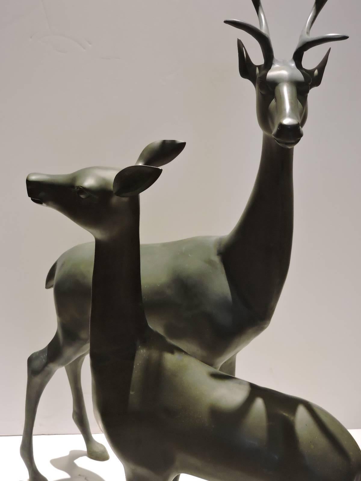 A perfectly proportioned great quality pair of sleek Hollywood Regency large brass deer statues in beautifully aged original dark bronzed verdigris patina, circa 1970. Stag measures 50 inches high x 24 inches wide x 12 inches deep / doe measures 33