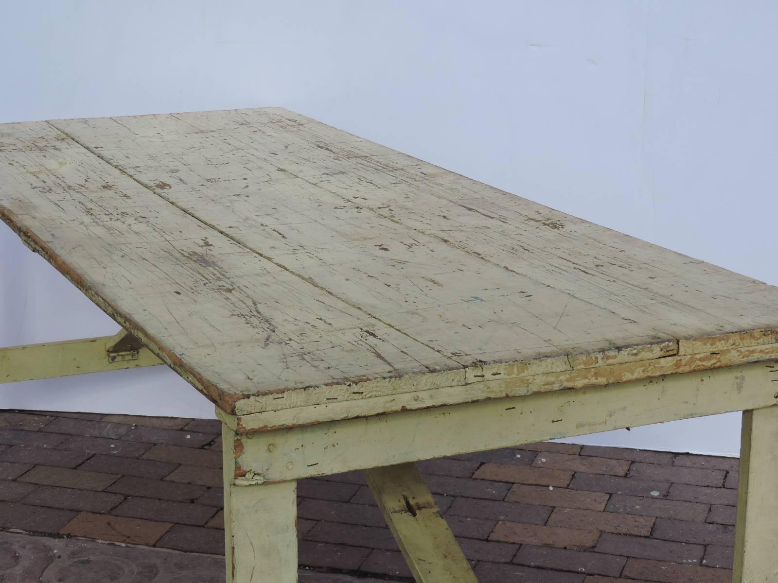 Folding collapsible leg farm harvest Grange work dining table in beautifully aged worn old pale yellow painted surface. A very versatile designed table perfect for indoor or outdoor dining as the legs fold under tabletop for easy transport and