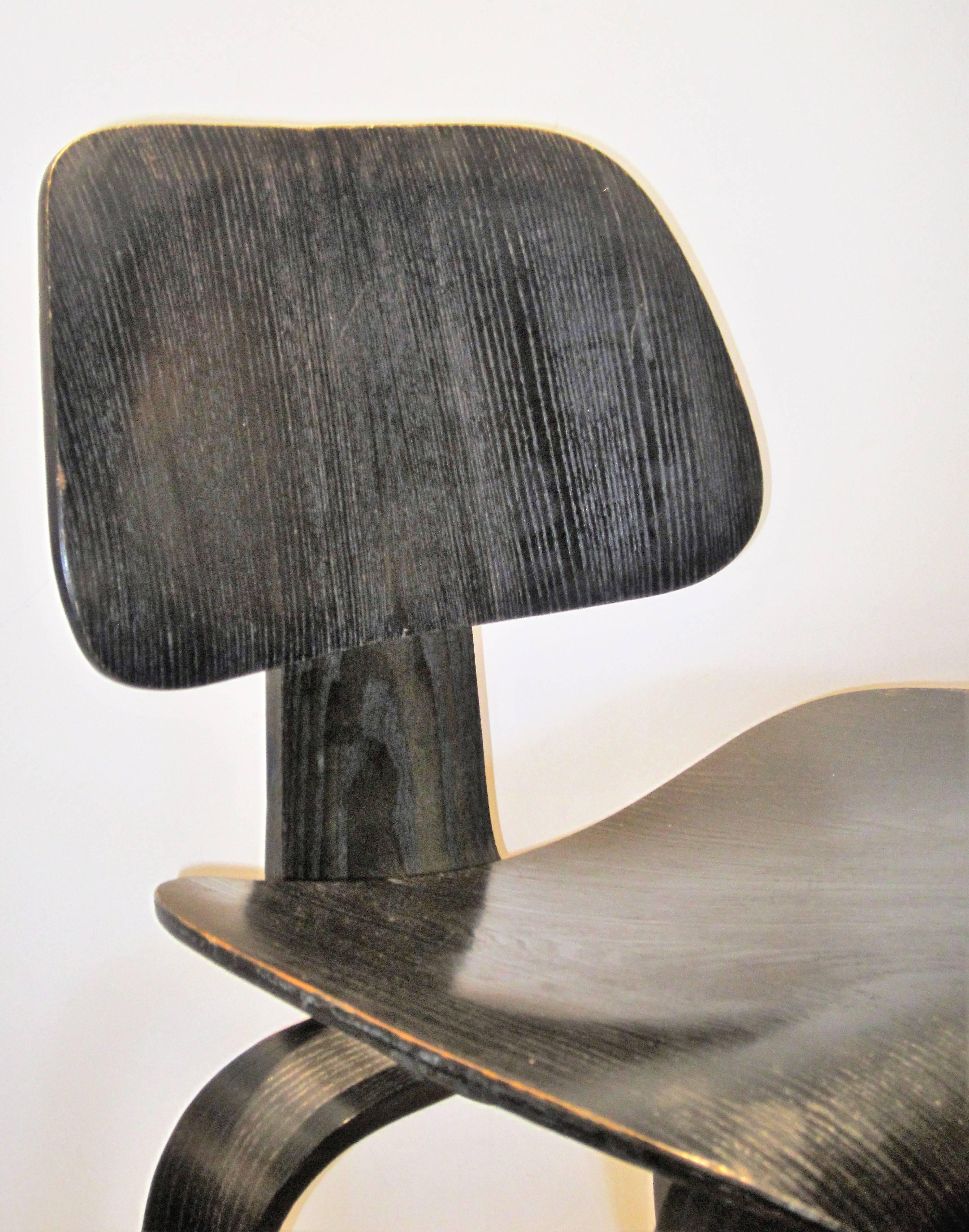 An early black aniline Eames DCW chair in all original very good vintage condition with nicely aged surface color.  Charles Eames Design for Herman Miller silver foil label on underside and four - two - five screw arrangement (see picture 8) circa
