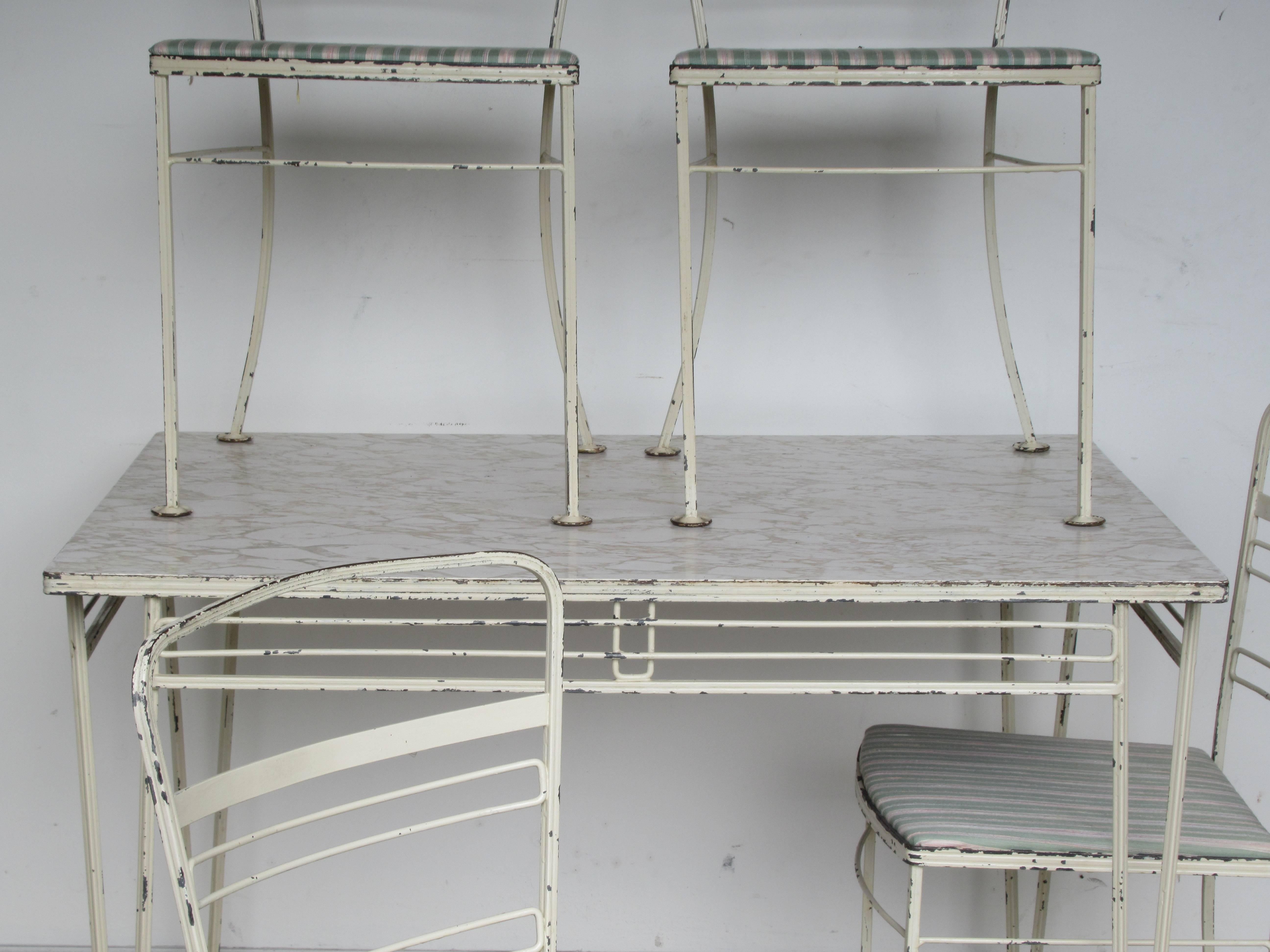 Mid-20th century modernist wrought iron patio set consisting of four chairs and one table. All pieces with very fine precisely detailed metalwork in old worn white painted surface.. A great looking hard to find early set attributed to John