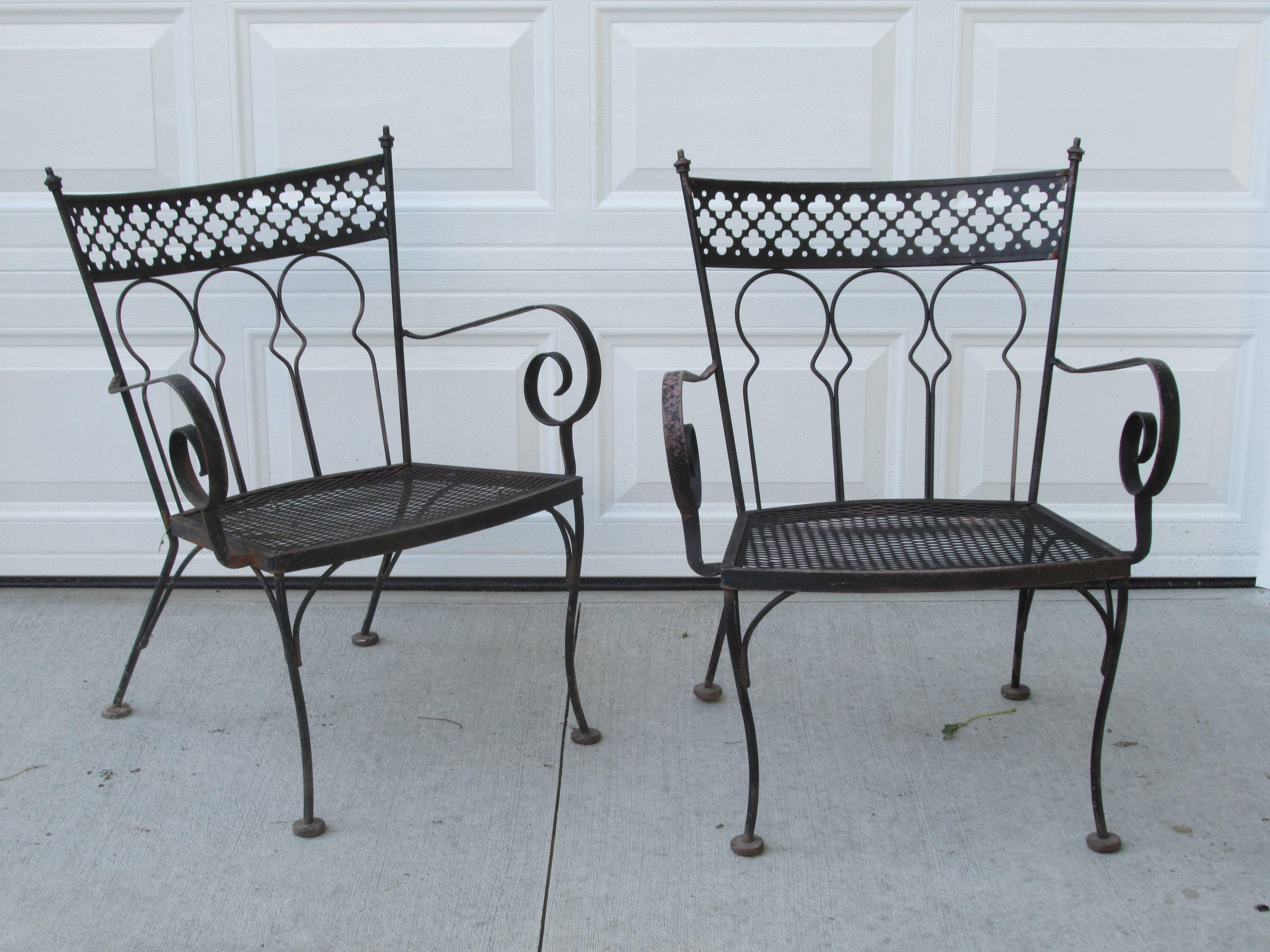 A great looking seven piece high style Gothic modernist wrought iron patio dining set consisting of four side chairs, two arm chairs and one rectangular table - all in nicely aged worn old black surface revealing underlying salmon color. Attributed