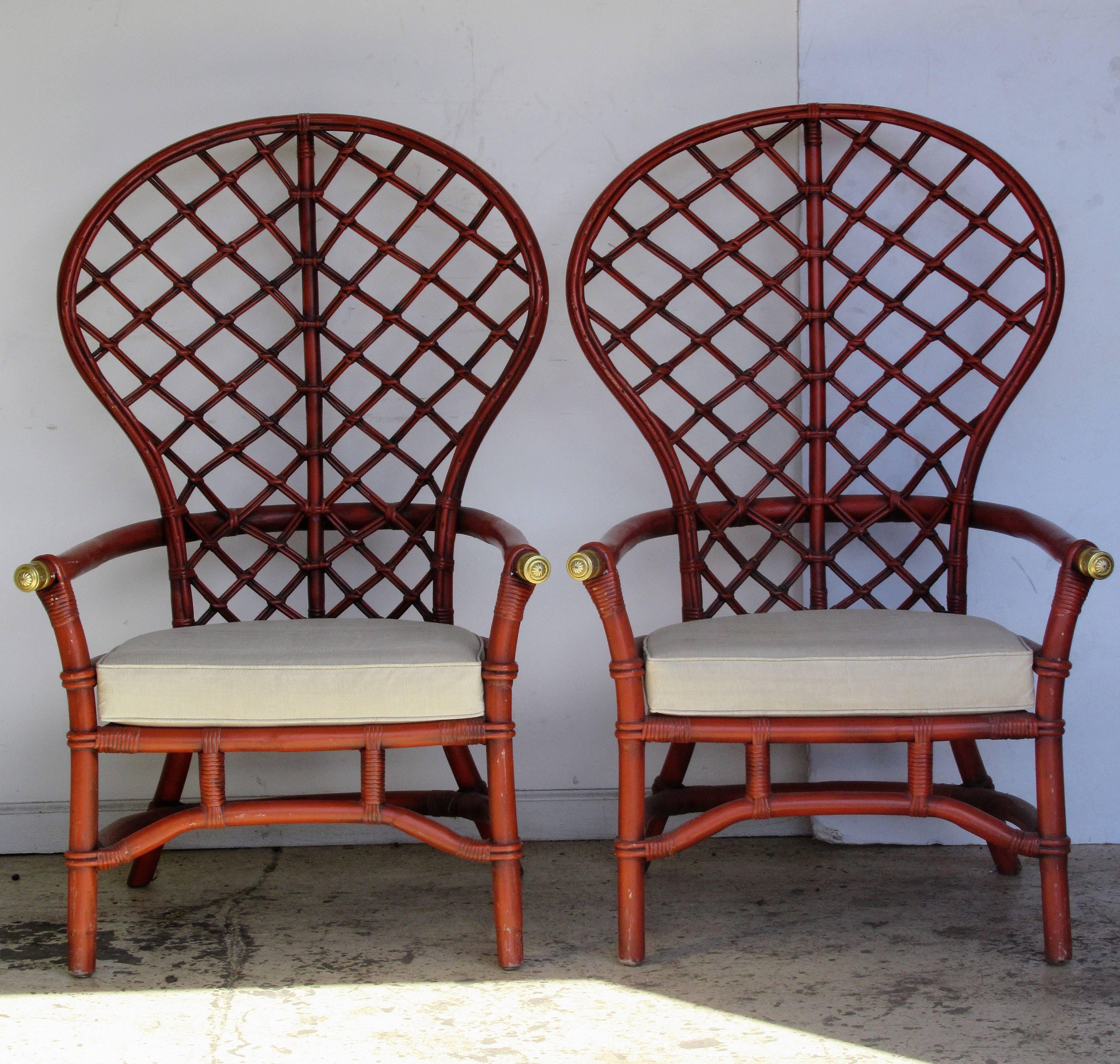 A pair of large-scale tall balloon back rattan armchairs fitted with decorative brass caps on arm ends. Both chairs in the most beautiful original glowing Chinese red stain painted finish. In the style Jean Royere / Chinese Chippendale, circa 1960.