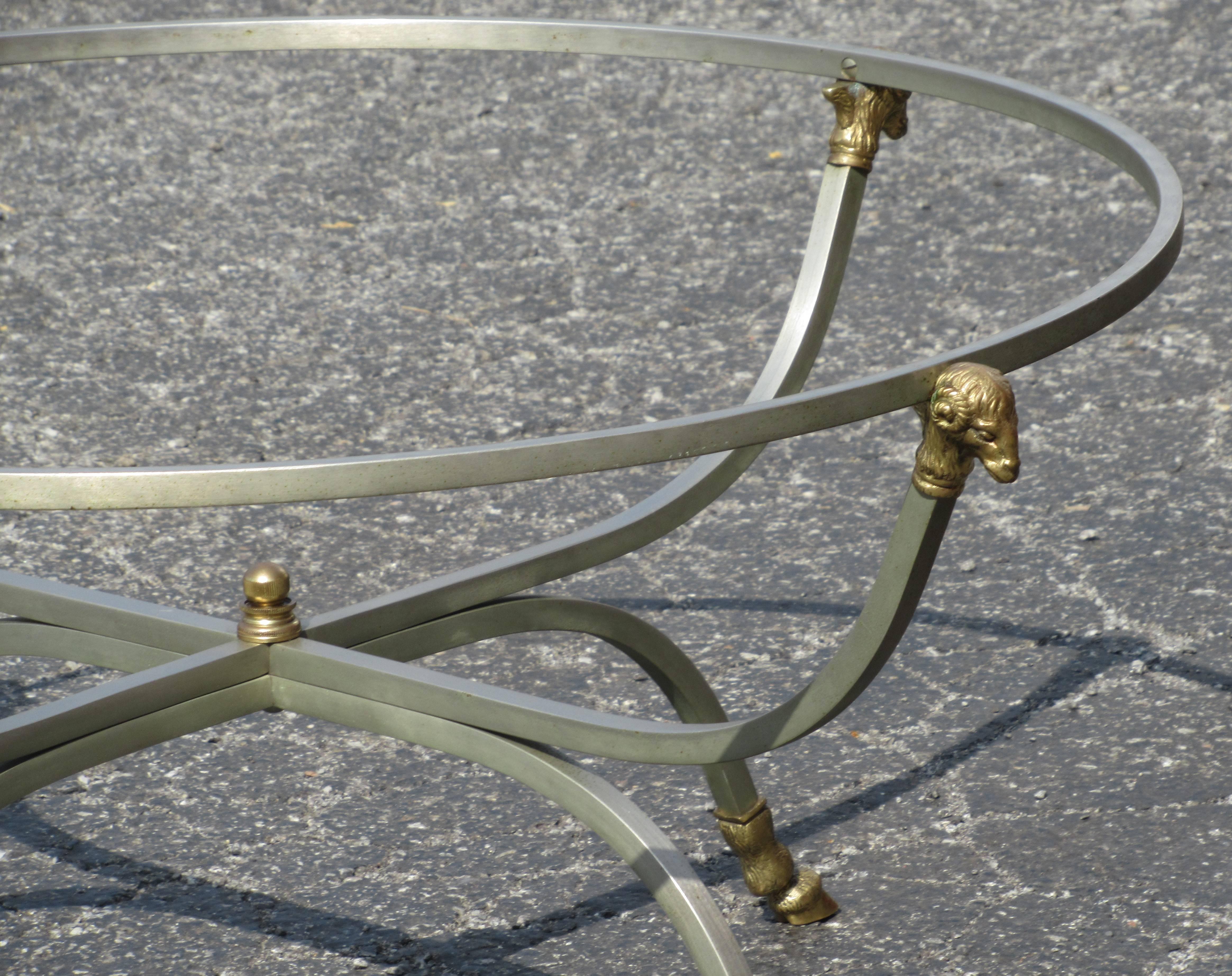 A neoclassical style steel cocktail coffee table with gilt brass bronze ram's heads at circular top / the curved legs with central brass ball finial ending in finely detailed brass bronze cloven hoof feet. Very good quality. In the style of Maison