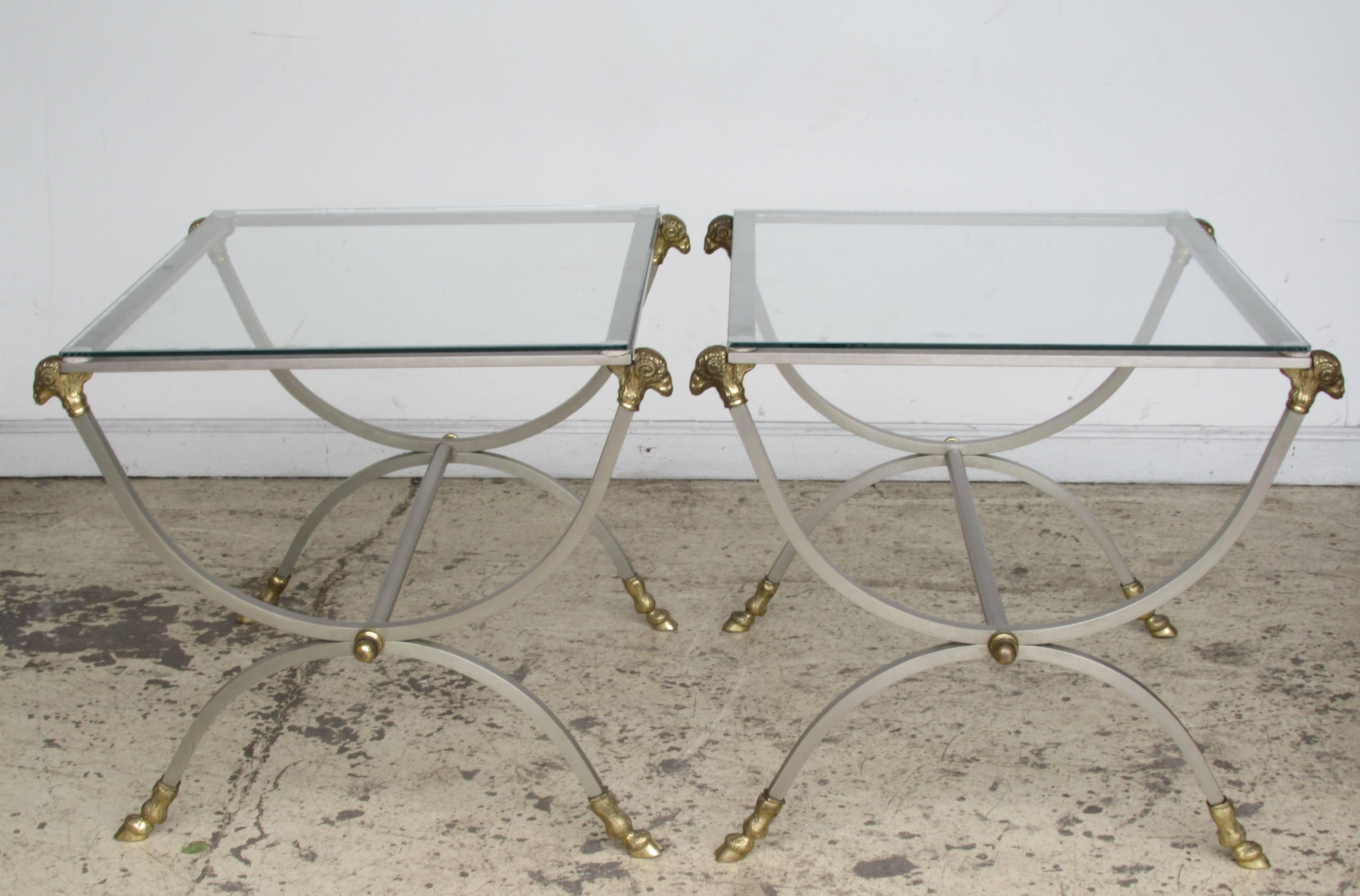 Pair of neoclassical style glass top steel tables with gilt brass bronze ram's heads and cloven hoof feet in the manner of Maison Jansen, made in Italy, circa 1960.
